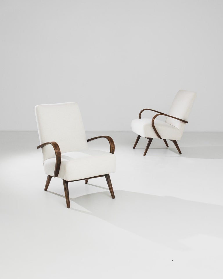 Bentwood upholstered armchairs by Czech furniture designer J. Halabala, circa 1950. A Mid-Century Modern silhouette, re-upholstered in a natural white. The cushioned seat is parenthesized by the dramatic swoop of the bentwood armrests; the neutral