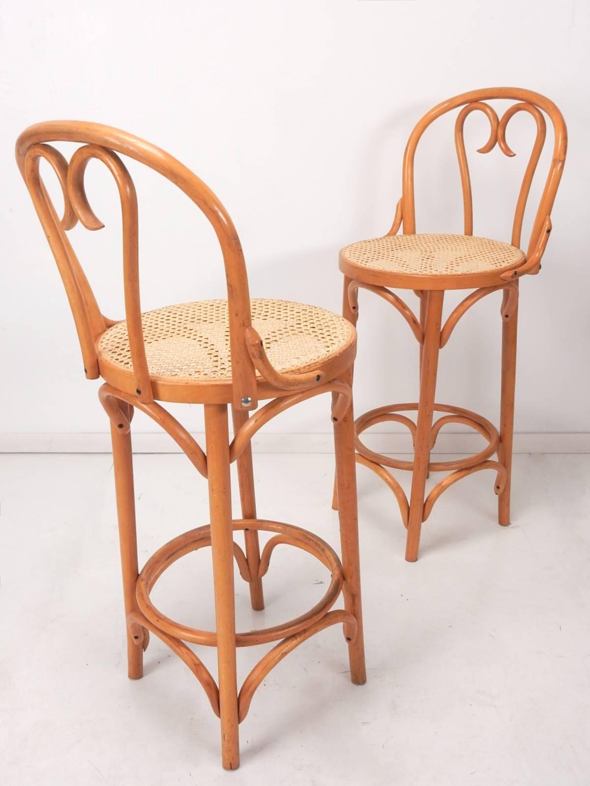 Set of four mid-20th century Thonet style bentwood cane bar stools with back rests.
Tall, counter height stools with footrest. 
All four are in very good condition, solid with no issues.
Cane seating is solid, free of holes or tears.
Nice golden