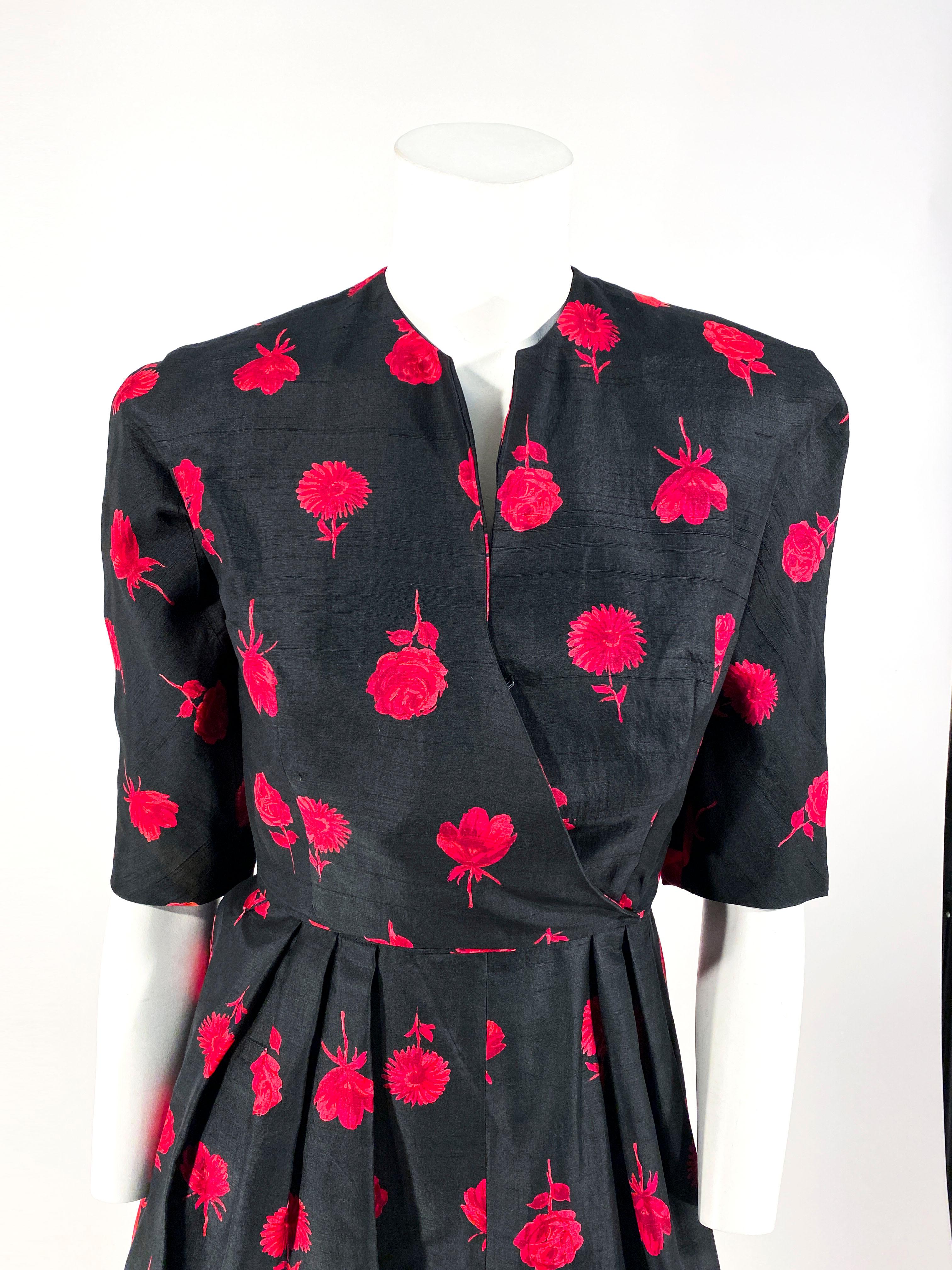 1950s I. Magnin black with red floral printed raw silk dress with a matching bolero jacket. The dress has structured shoulders, a sleeveless bodice, and a slight plunge v-neckline. The skirt is pleated at the waist creating a modestly full skirt.