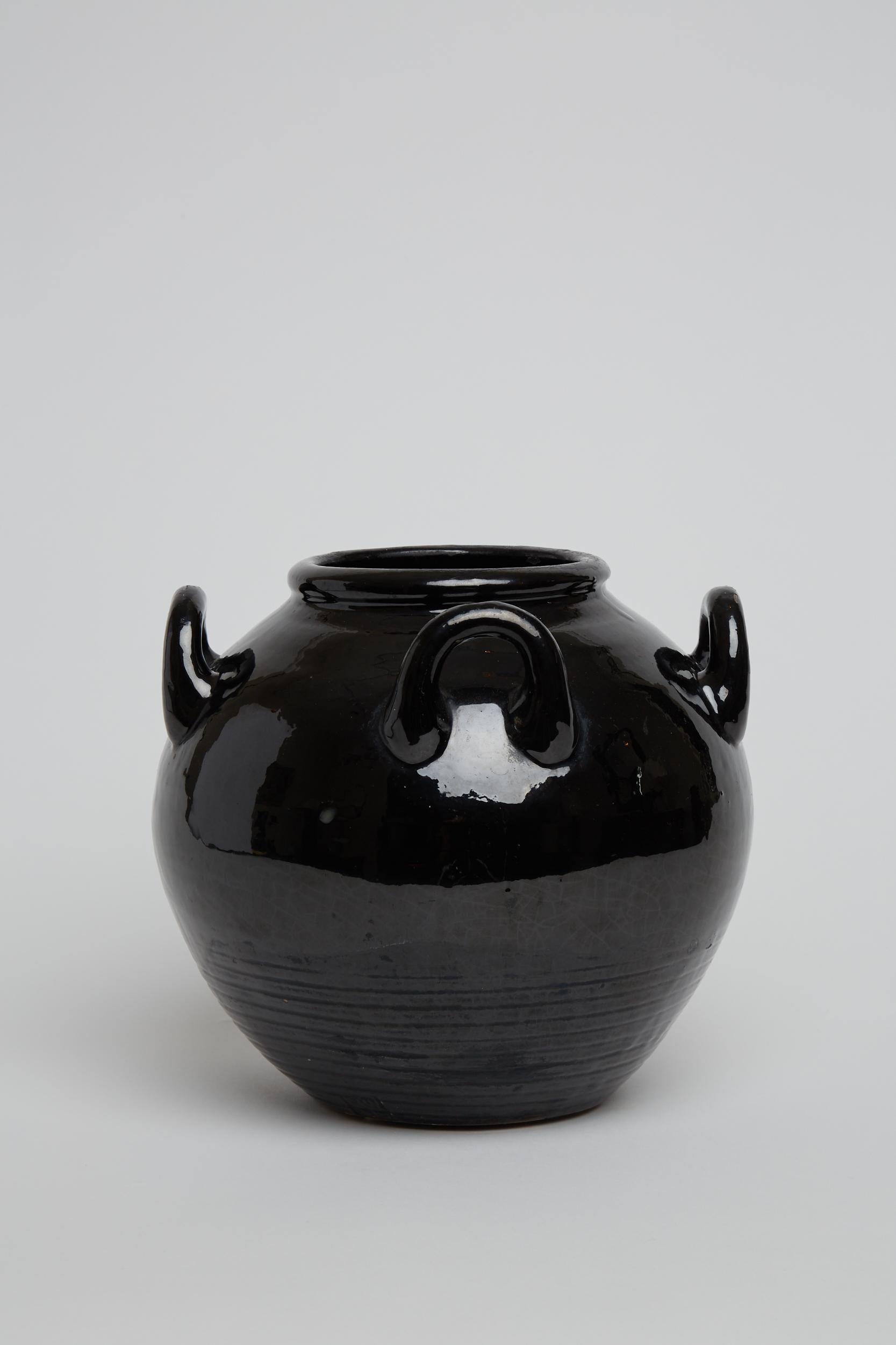 A black wet glazed ceramic vase with four handles.
France, Circa 1950.