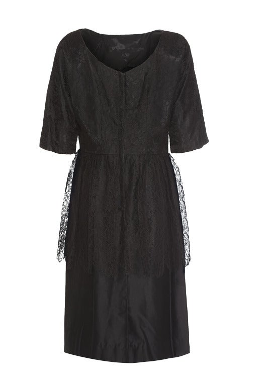 This enchanting 1950s black chantilly lace cocktail dress is unlabelled and we believe it to be American in origin. It is a silk cotton blend with a chantilly lace overlay and features a pleated satin sash waistband with a diamanté pin brooch