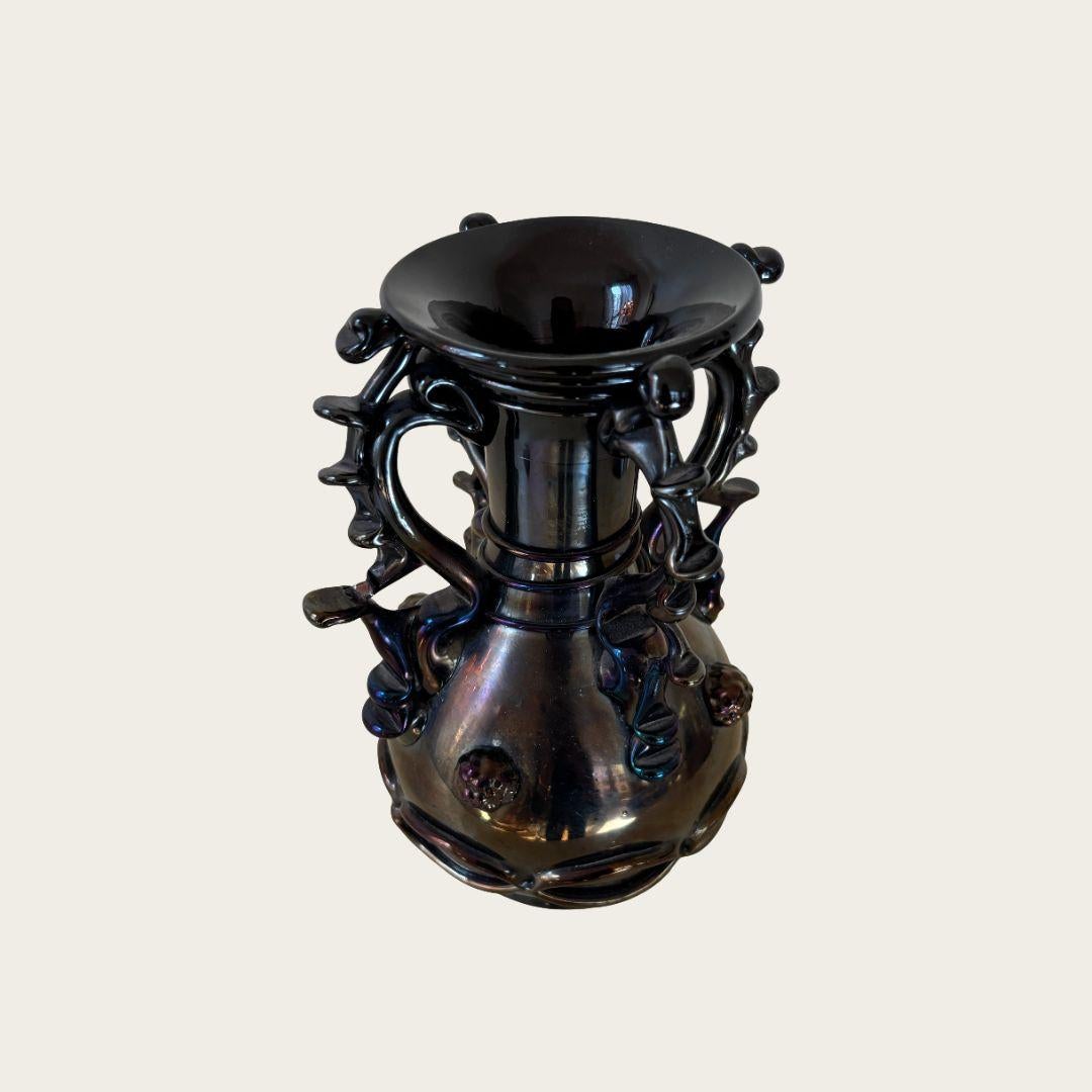Ce vase en verre de Murano noir irisé des années 1950 présente des poignées sculpturales et des décorations en verre soufflé sur l'ensemble de sa surface. Son design unique et sa finition chatoyante en font un ajout saisissant à tout espace.