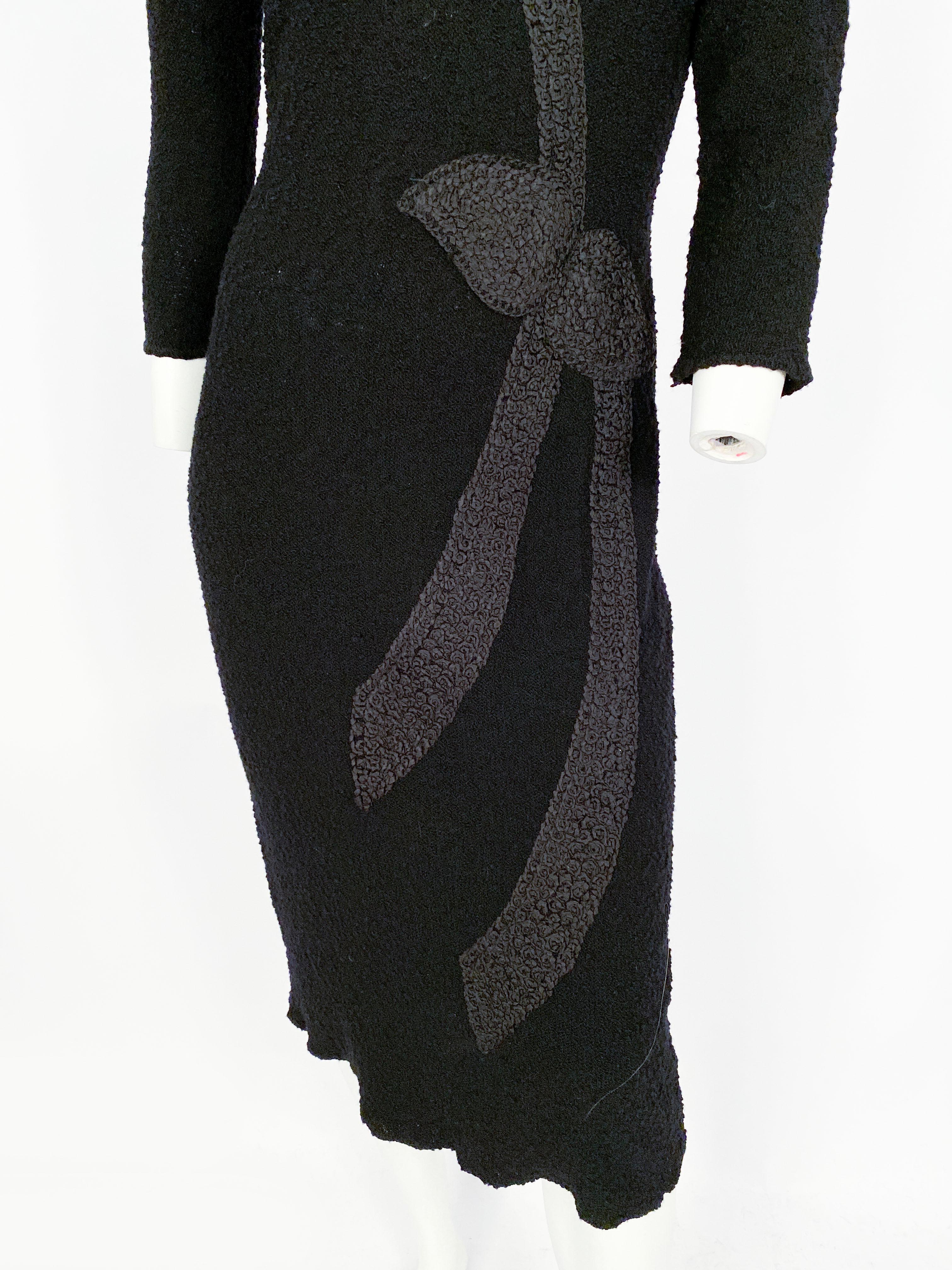 1950s black knit dress with 3/4-length sleeves, modified raglin shape, asymmetrical ribbon work that is finished to look like a dimensional tied bow to complement the v-neckline. Since this dress is knit, it has a considerable amount of stretch. 