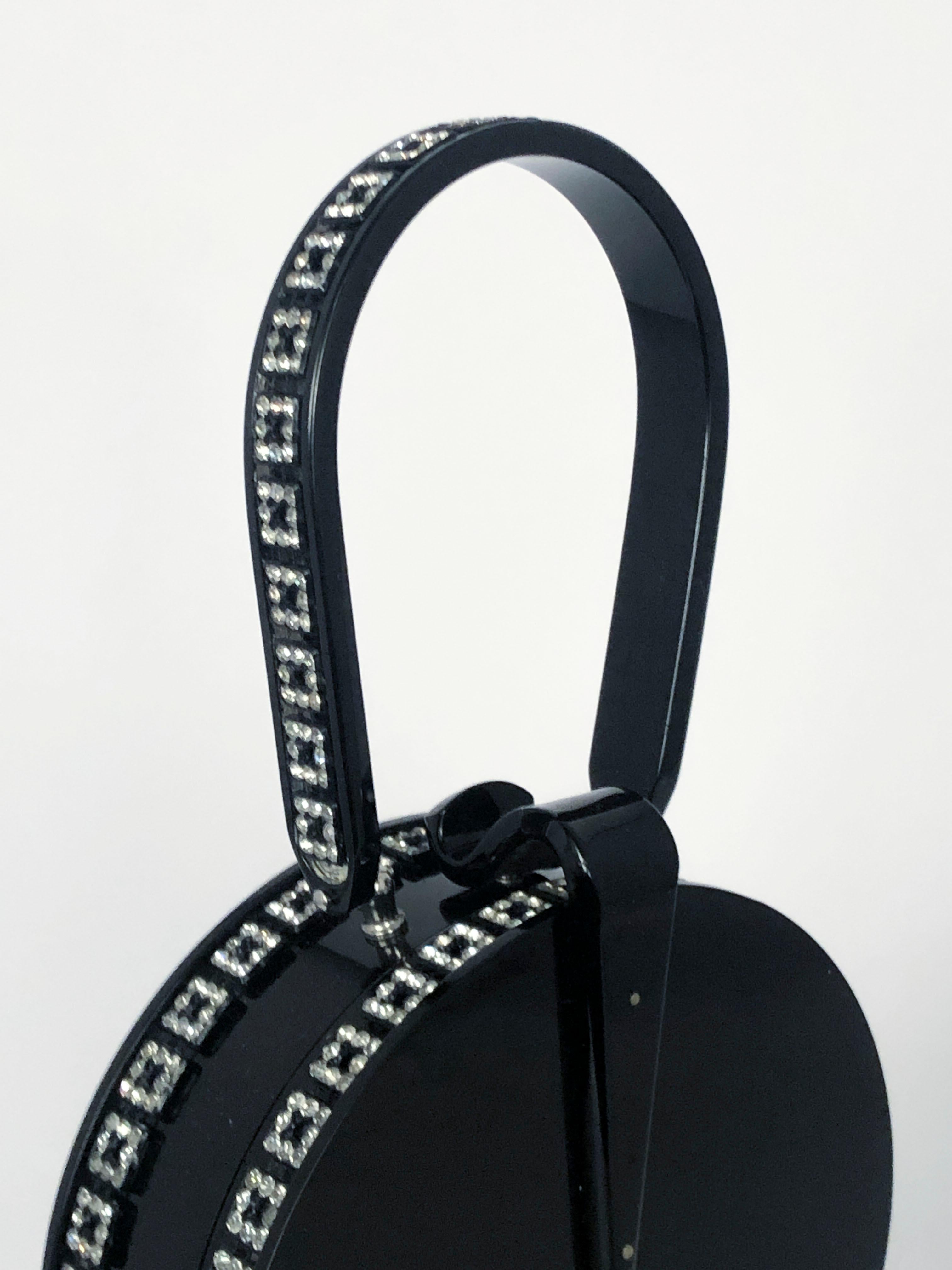 Black Lucite handbag accented with a clear rhinestone border configured in a geometric pattern. The interior is fixed with a large circular mirror attached to the side of the handbag.