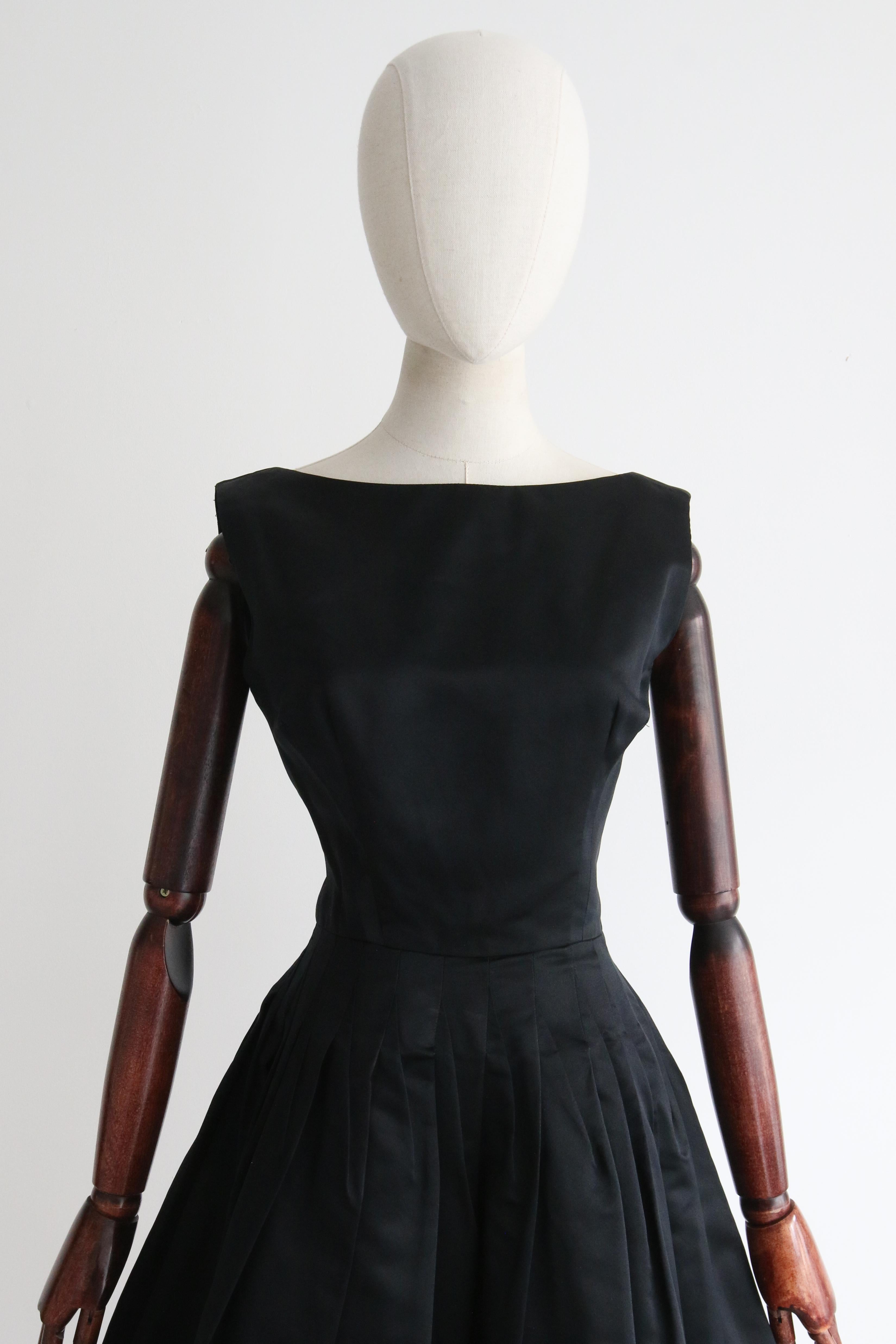 This truly mesmerising 1950's couture dress, rendered in a sumptuous black satin and accented by angular pointed seams, is just the piece to add to your timeless capsule collection.

The bateau neckline of the dress is framed my medium shoulder