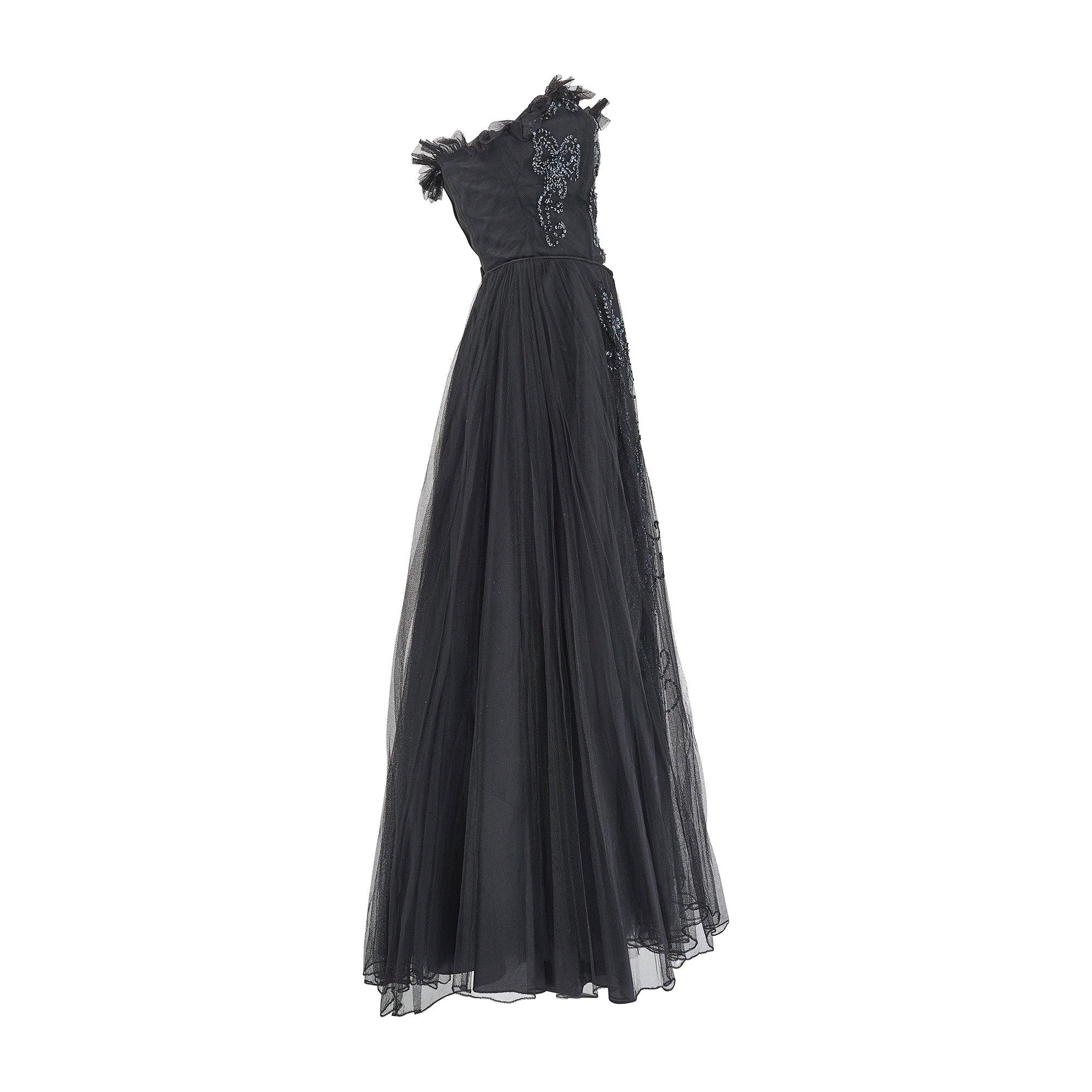 This 1950s black tulle gown was created by an unknown British couture salon, and is very reminiscent of Pierre Balmain's haute couture designs circa 1955. A dressy cocktail gown from this era, it is adorned with playful details that make it special.