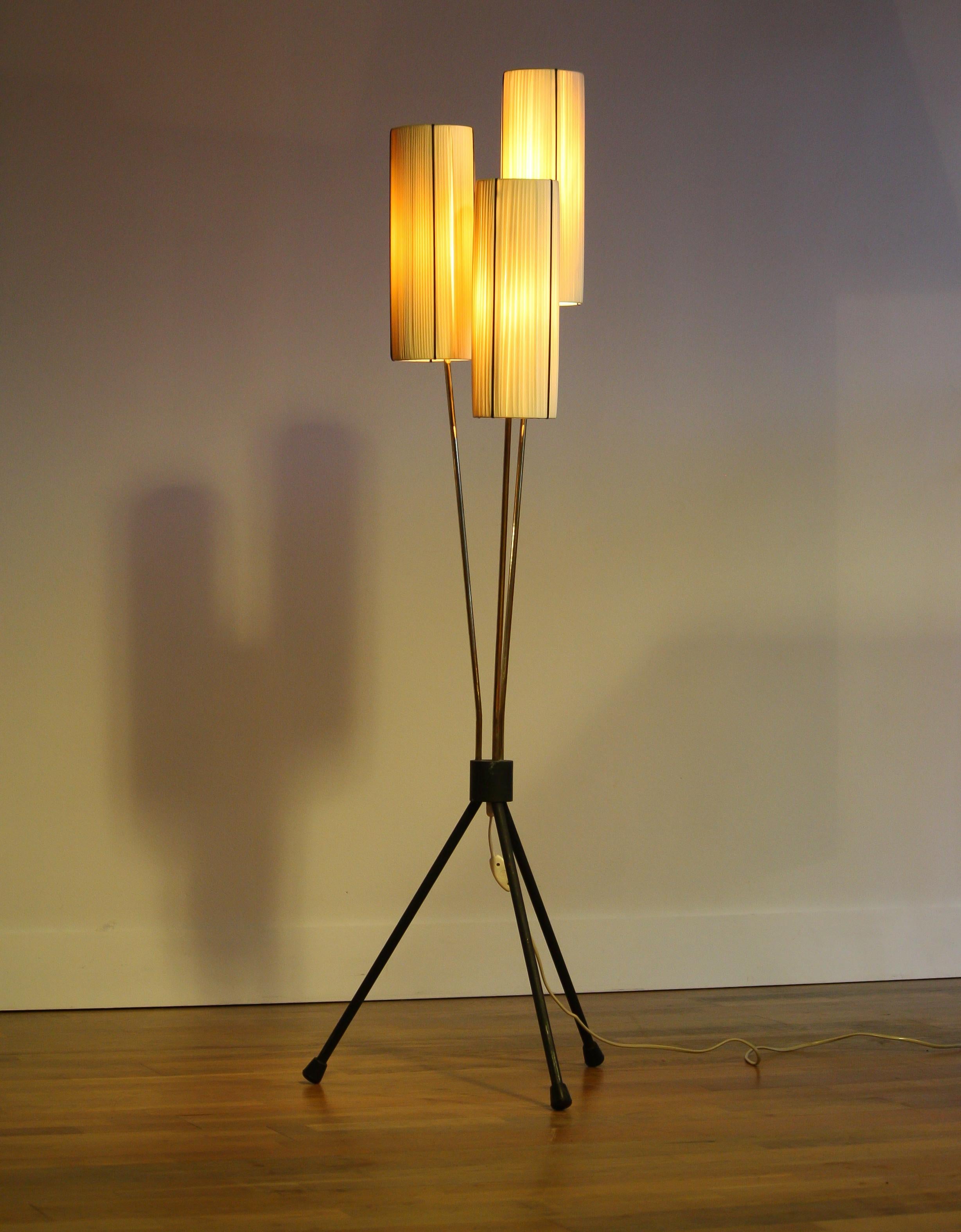 Typical 1950s floor lamp with two off-white and one salmon polyester fabrics covers.
The caps are lined with black cords.
The lamp stands on a metal three-leg rest covered with black polyester.
The overall condition is good. Technically