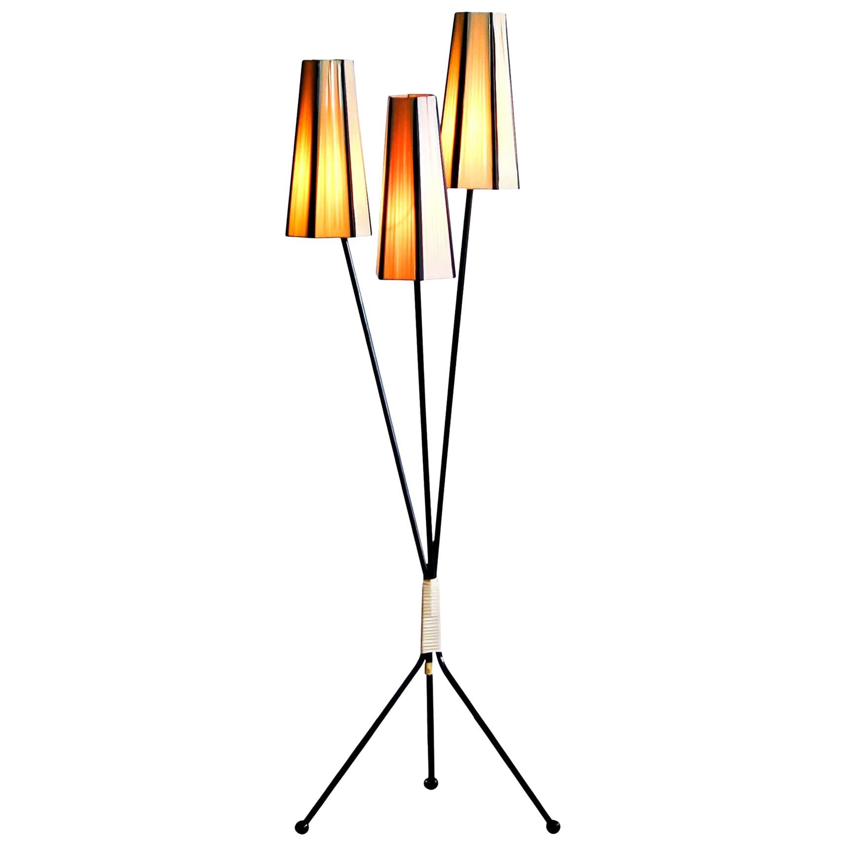 Typical 1950s floor lamp with two off-whites and one salmon polyester fabrics covers.
The caps are lined with black cords.
The lamp stands on a metal three-leg rest covered with black polyester.
The overall condition is good. Technically