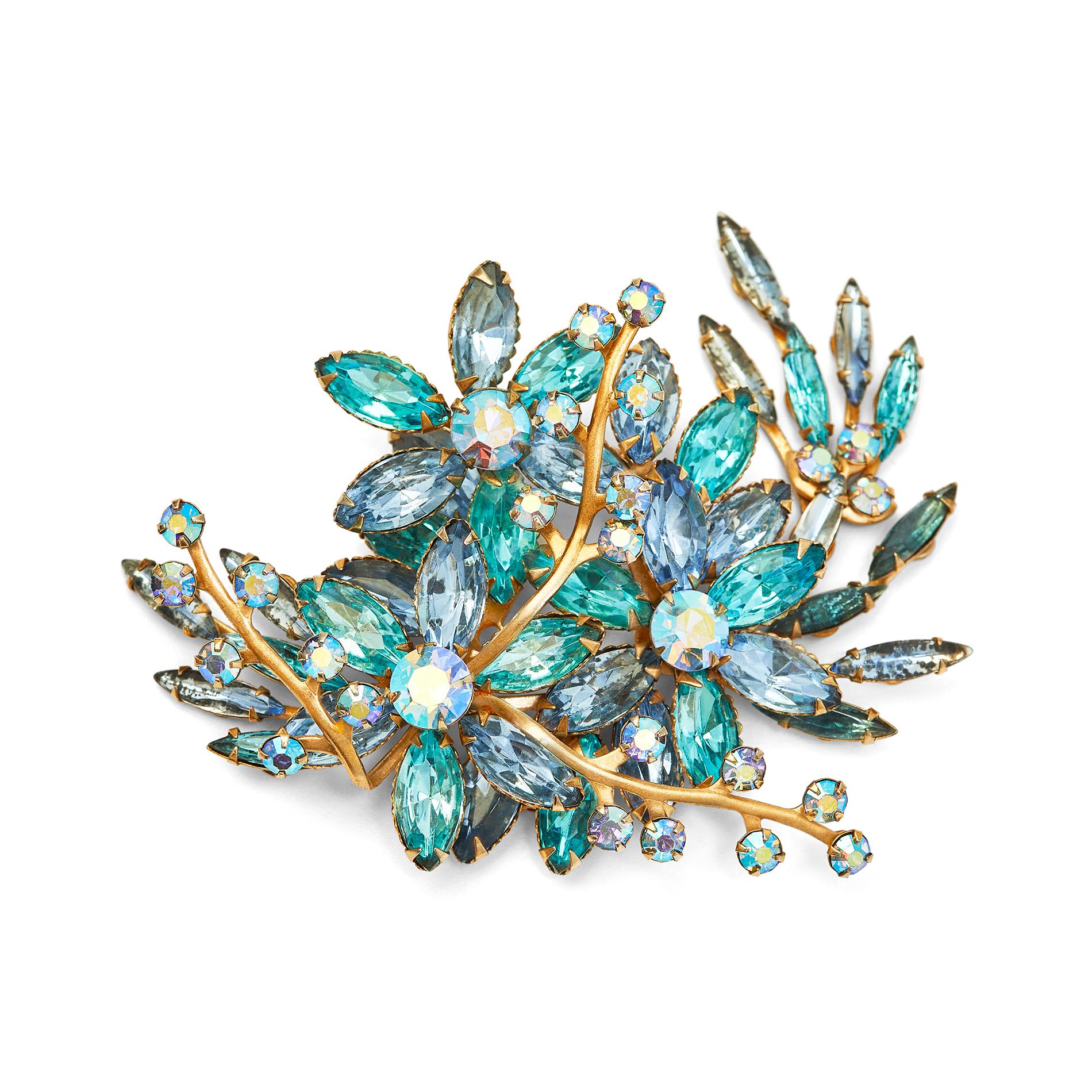 This impressive sized 1950s or early 1960s brooch features a very large spray of flowers and foliage in a mixture of sparkling powder blue and turquoise stones, all individually prong set. Each of the three flowers has five petals and a central