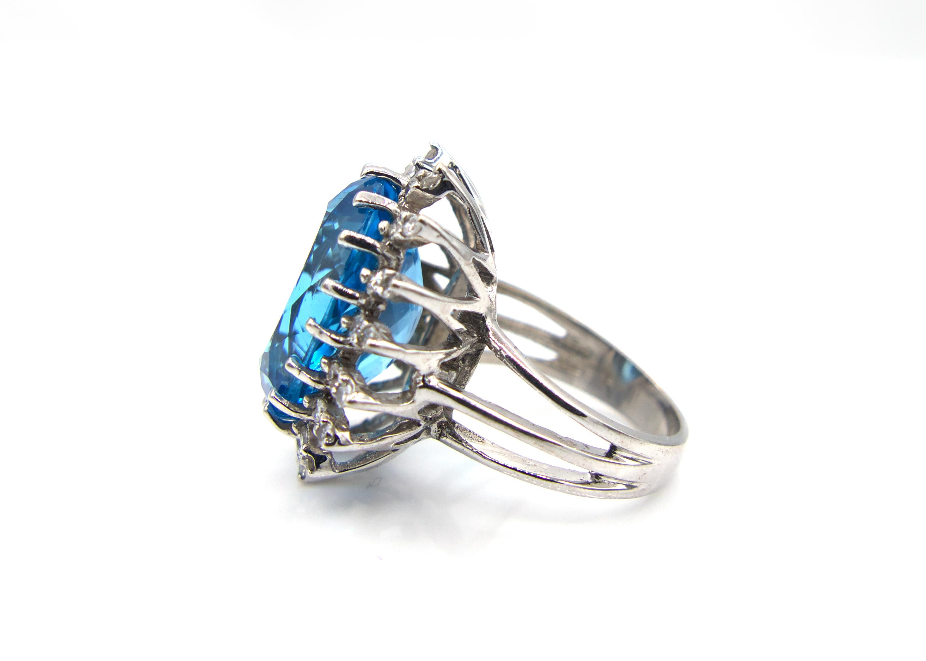 This spectacular 1950s ring features a large oval Blue Topaz center stone that weighs in at 20 Carats with 32 single round-cut diamond clusters, weighing at 1 Carat total, surrounding it on a vintage setting. The classic open cage band is made of