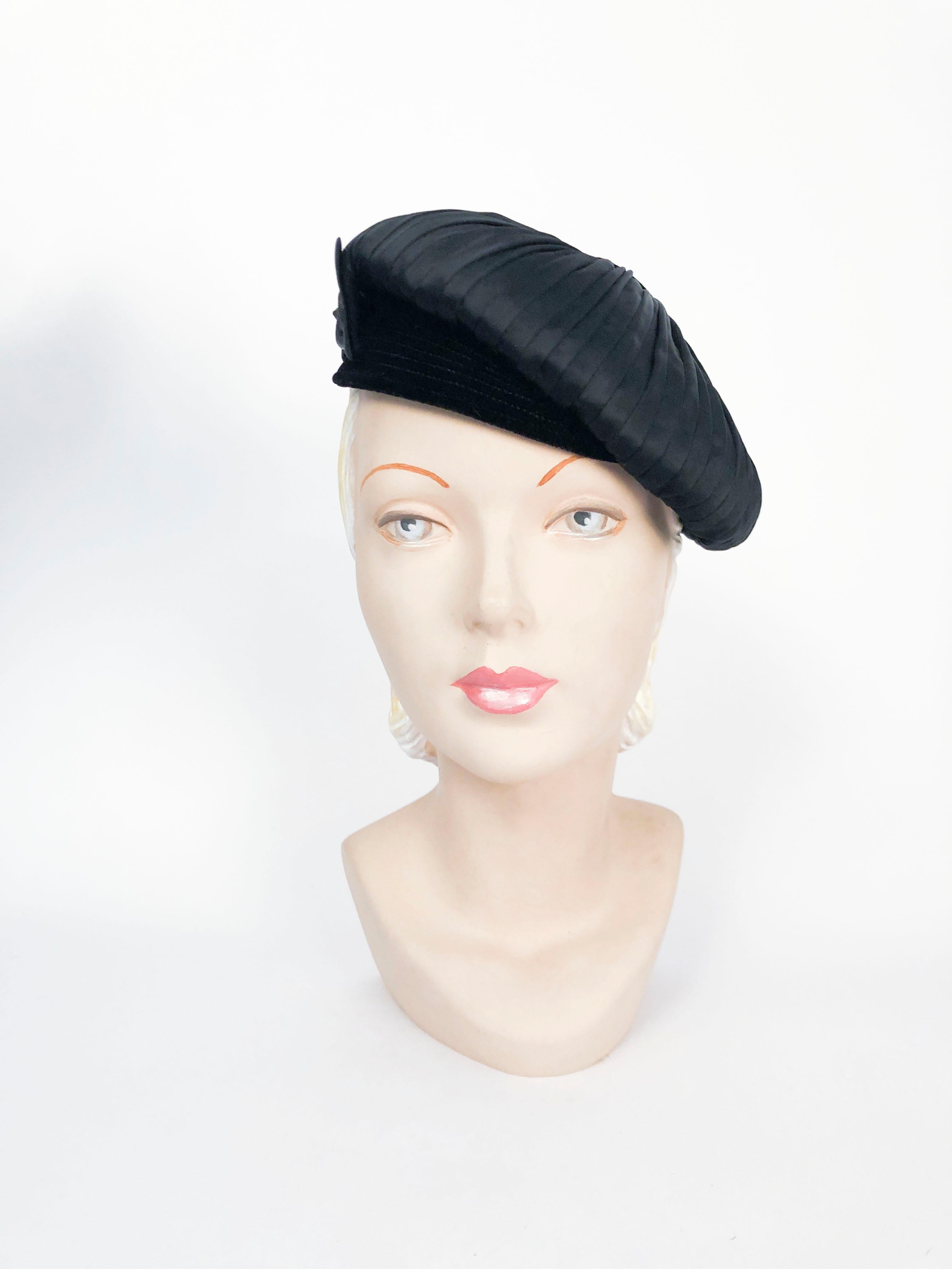 1950s Bonwit Teller black cap/tam that is hand-gathered satin with a black velvet button and bill. Accented with satin bow and articulating button. 