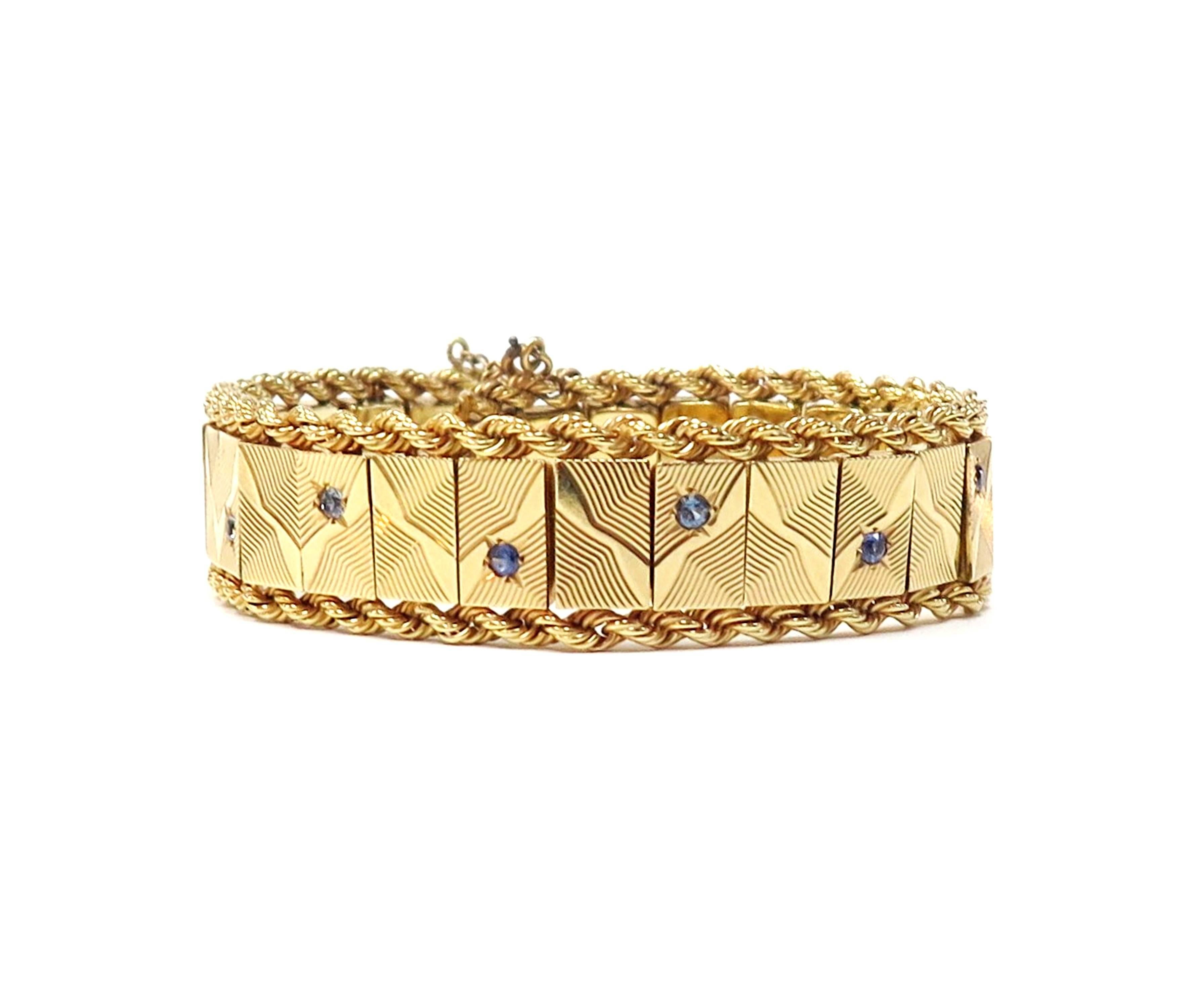 A wavy textured design on rectangular panels is punctuated in 1/2 inch intervals by bright blue faceted round sapphires in this flexible bracelet rendered in rich 14K yellow gold and bordered on each side with rope chain. 

Has a safety chain.

