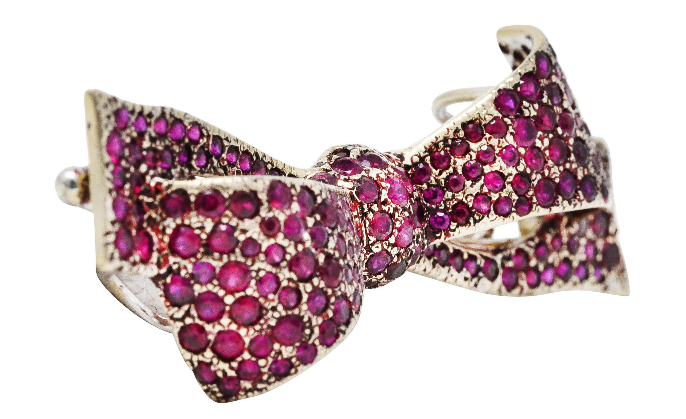Pendant brooch is dynamically formed as a ribboned bow - oriented East to West. Pavè set throughout by round cut rubies weighing in total approximately 5.00 carats. Very well matched in vivid strongly purplish red color with medium saturation. Pavè