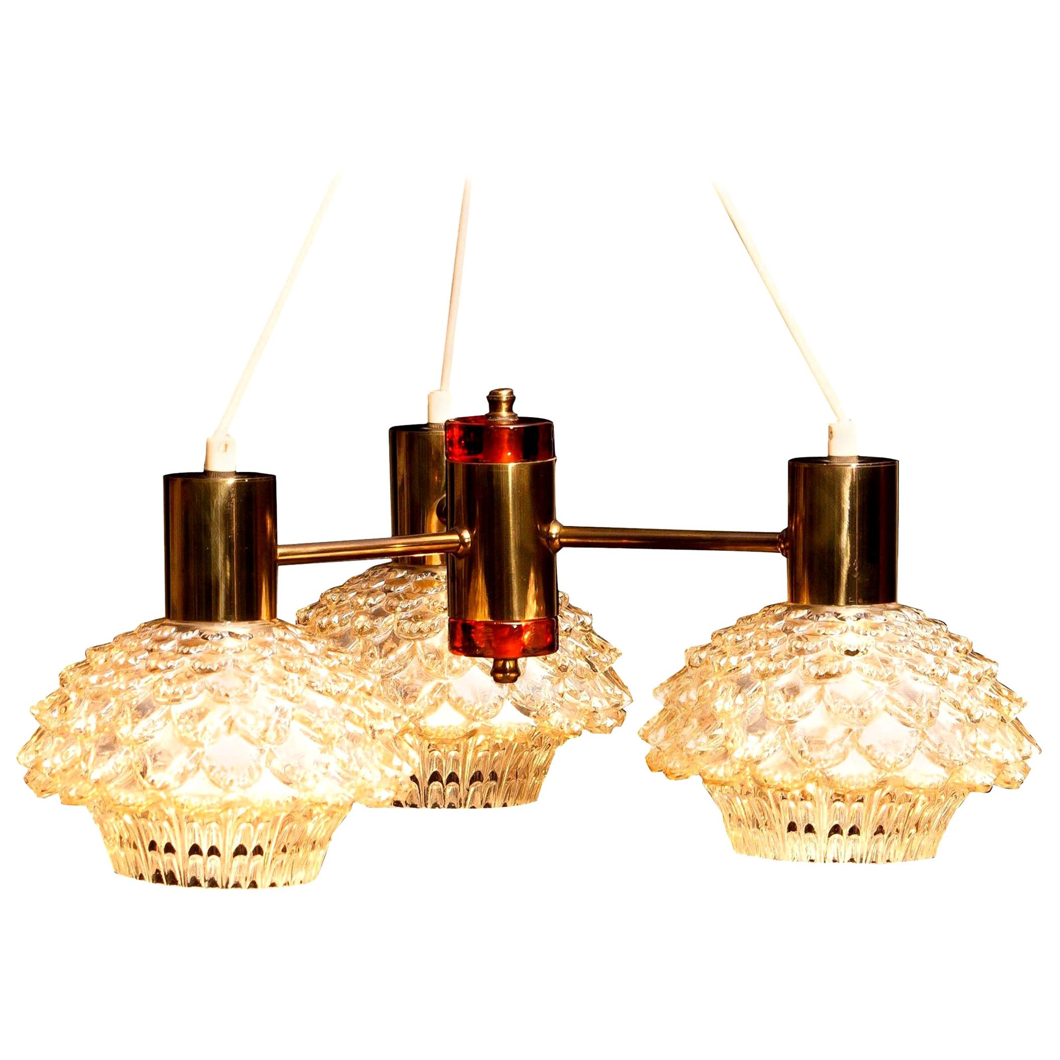 Beautiful chandelier designed by Carl Fagerlund for Orrefors, Sweden.
This lamp has three brass arms with amazing glass shades.
In the middle a brass cylinder with on the top and bottom an amber glass element.
It is in a very nice
