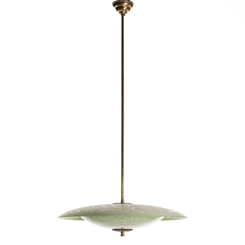 This playful piece consists of a brass frame connecting two unique frosted glass reflectors in green-tone.
The lower glass reflector is accented with a gold-colored ring and clear glass motifs. This mounts underneath a round, green frosted glass