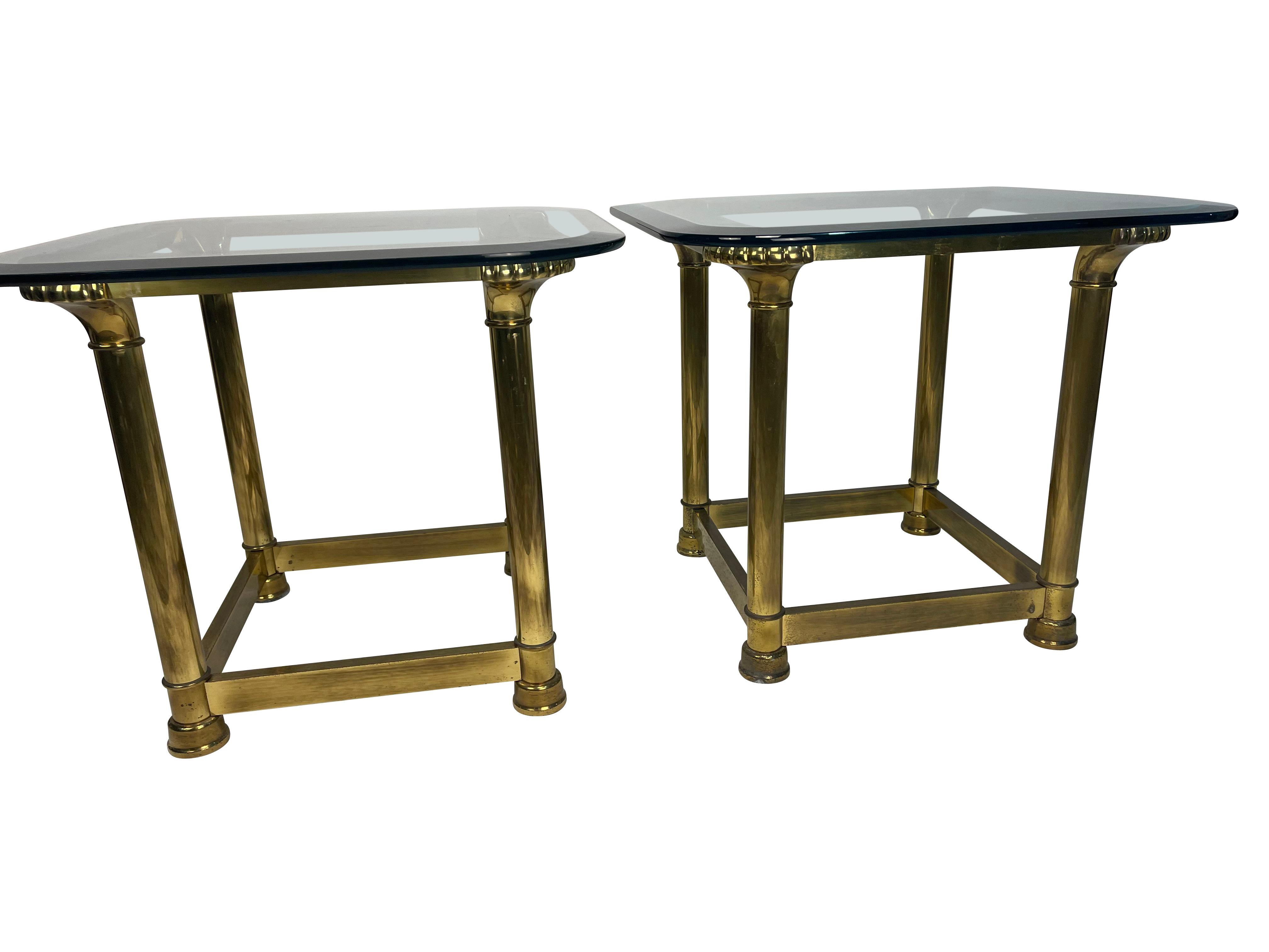 A pair of 1950s brass and glass top tables. Heavy, quality brass with scallop decoration at the four top corners visible through the heavy, quality, beveled glass tops.  Four-column legs ending in capped feet.  These are a lovely addition to any