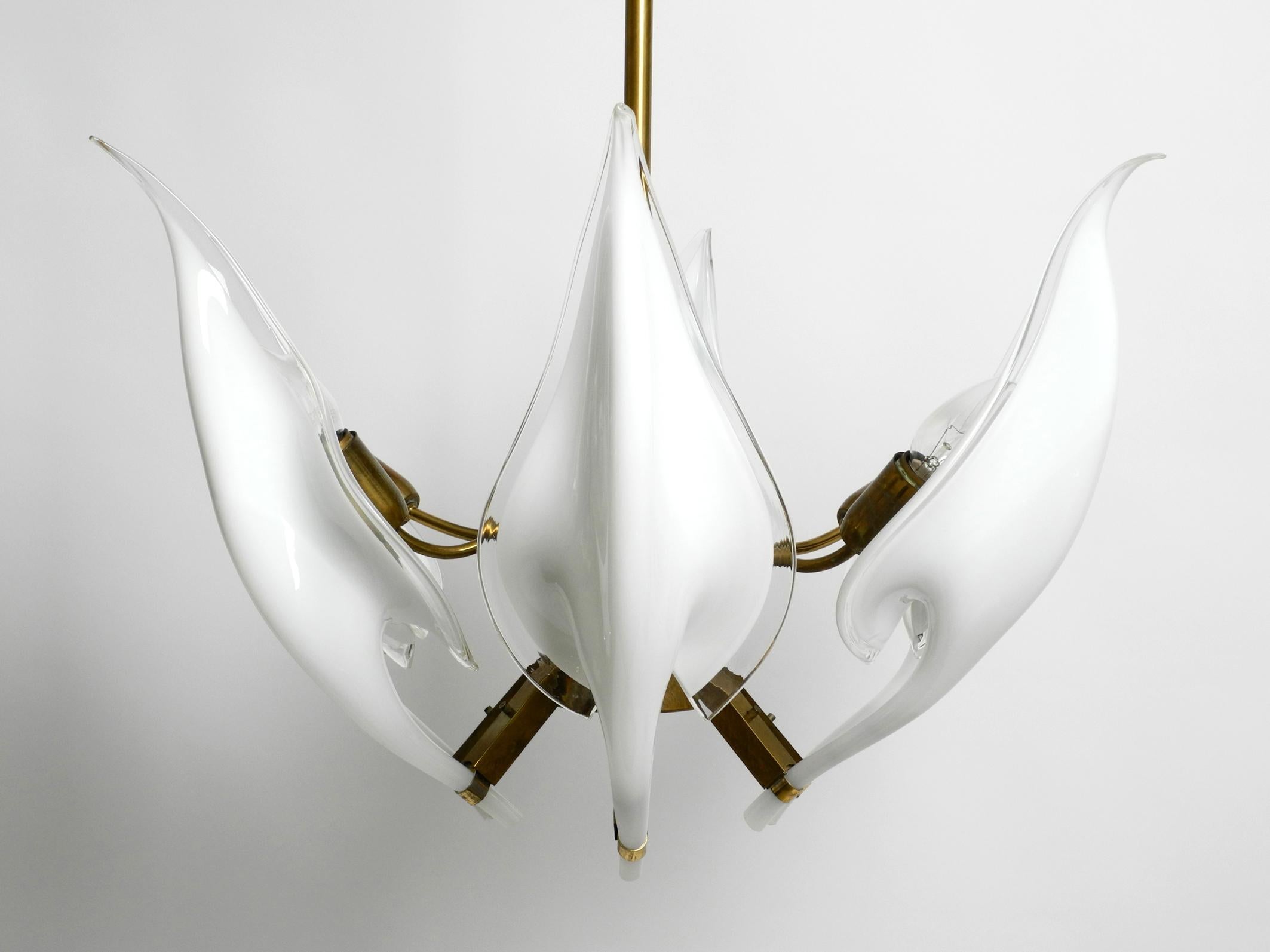 Schöner großer Messingkronleuchter aus den 1950er Jahren mit weißen bis transparenten Murano-Gläsern.
Entworfen von Franco Luce. Hergestellt in Italien.
Sechs lange, durchsichtige, weiße Gläser, die die Form eines Blütenblattes haben.
Jedes Glas