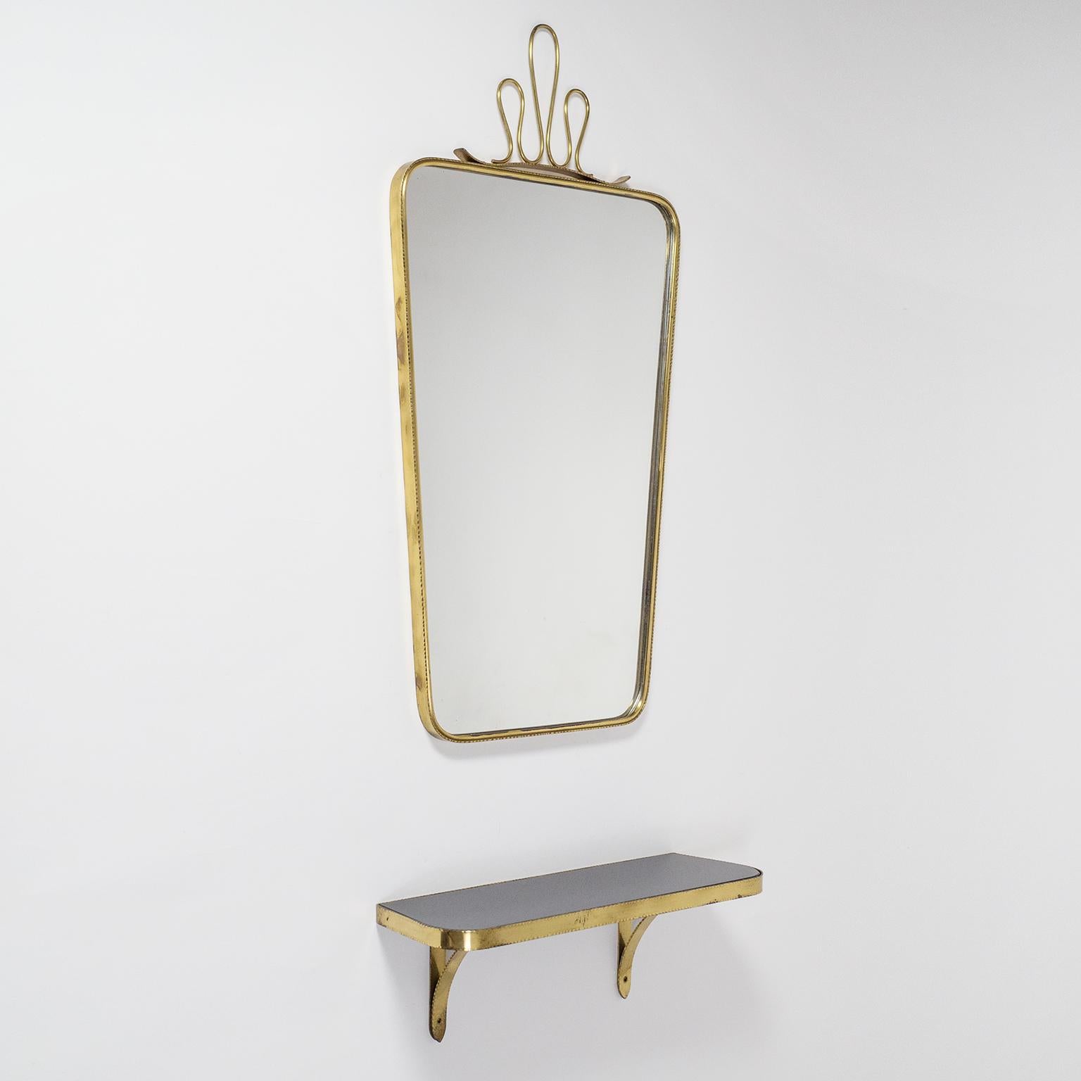 Charming 1950s brass wall mirror and console. Solid continuous brass frames with unusual hammered rims. The mirror with original glass has a large brass finial reminiscent of Gio Ponti designs. The wall console has a rare black opaline glass top.