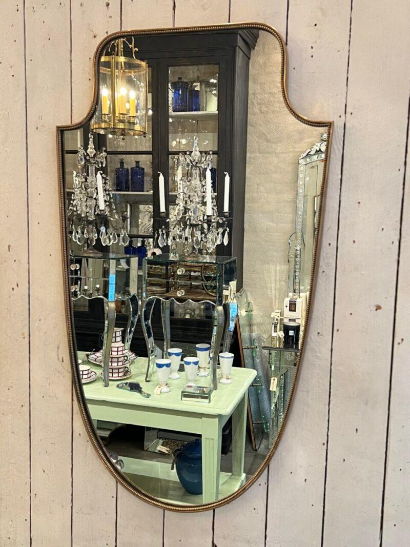Mid-century beautiful Italian brass mirror. Wonderful imaginative almost shield like form.

Original mirror glass, and stylistically related to the Gio Ponti’s famous designs. Extra ornamentation due to the charming beading around the edge.

The