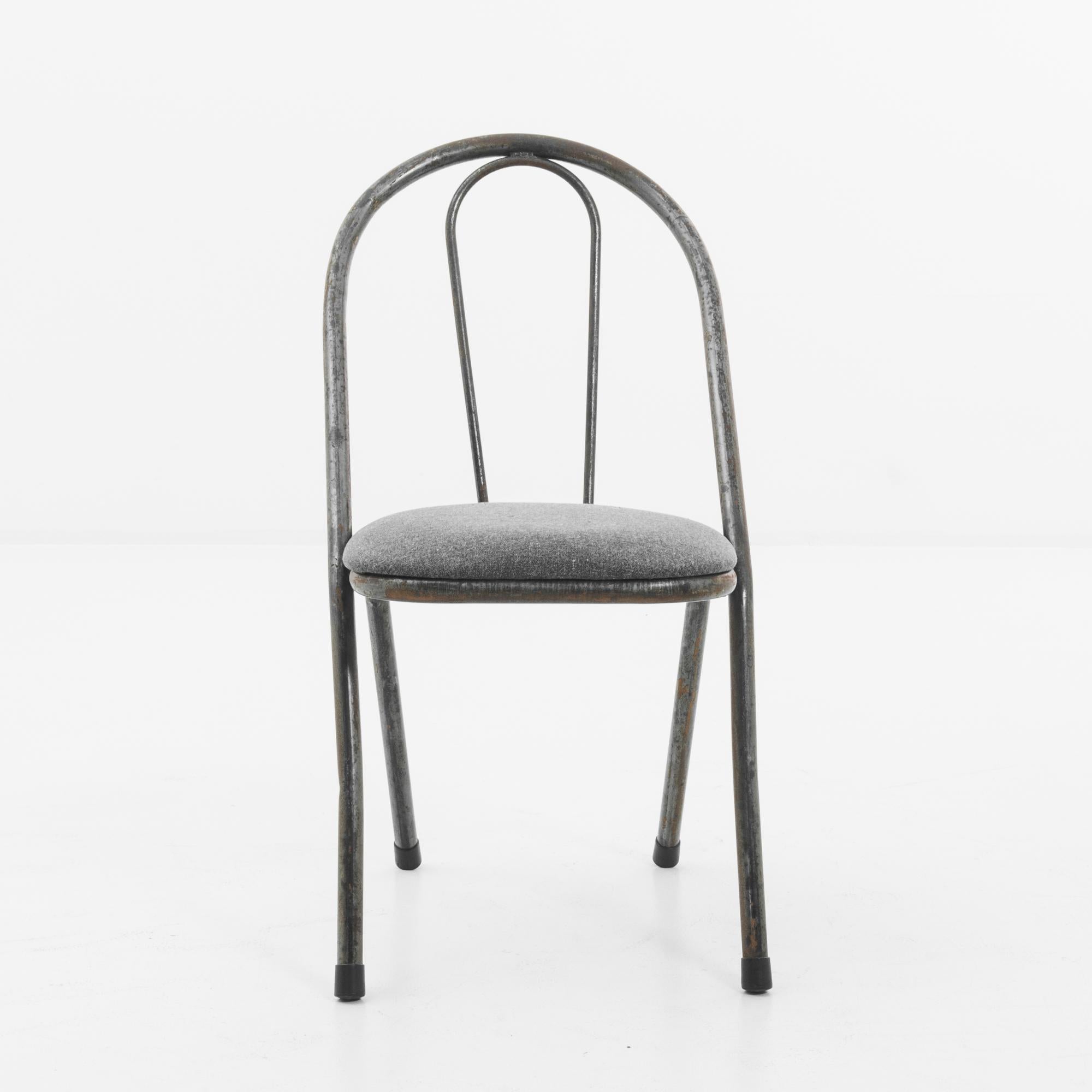 A metal chair from the United Kingdom, produced circa 1950. A chair’s chair, Windsor inflected; two main stalks of bent metal with rubber tipped feet curled around a soft cushion in a light charcoal gray. Hearkening to the flannel suits of the