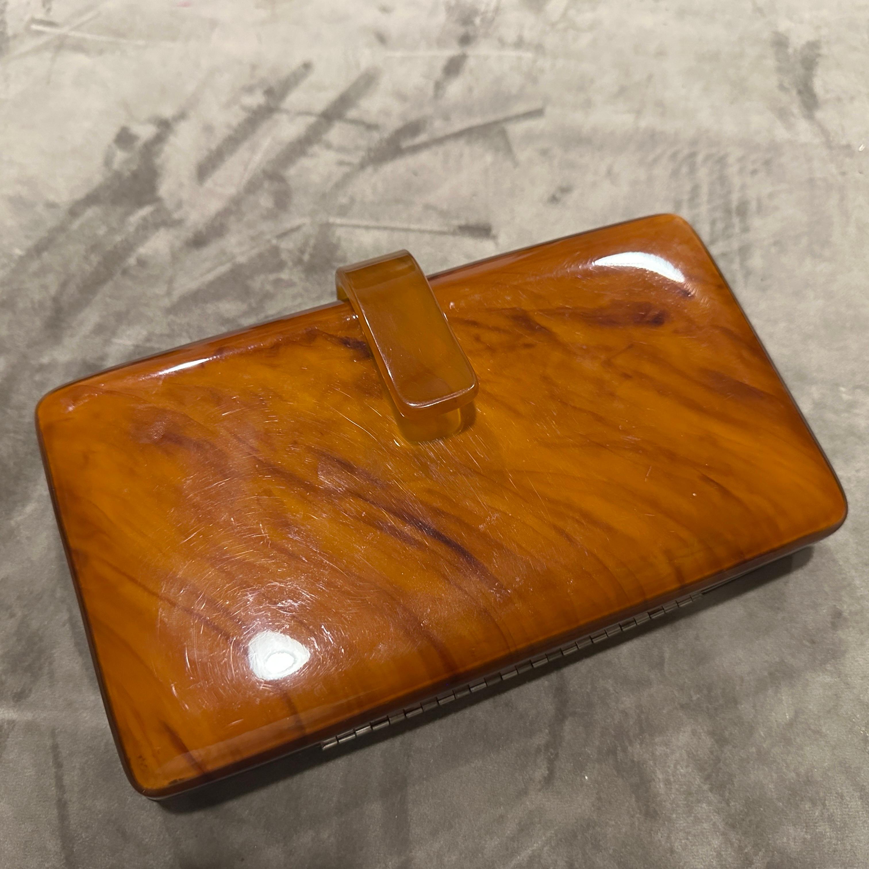 This piece is a beautiful example of mid-century design, combining the lustrous, rich tones of Bakelite with the classic elegance of genuine leather.
The exterior features a sleek, rectangular Bakelite body in a stunning amber-brown marbled finish.