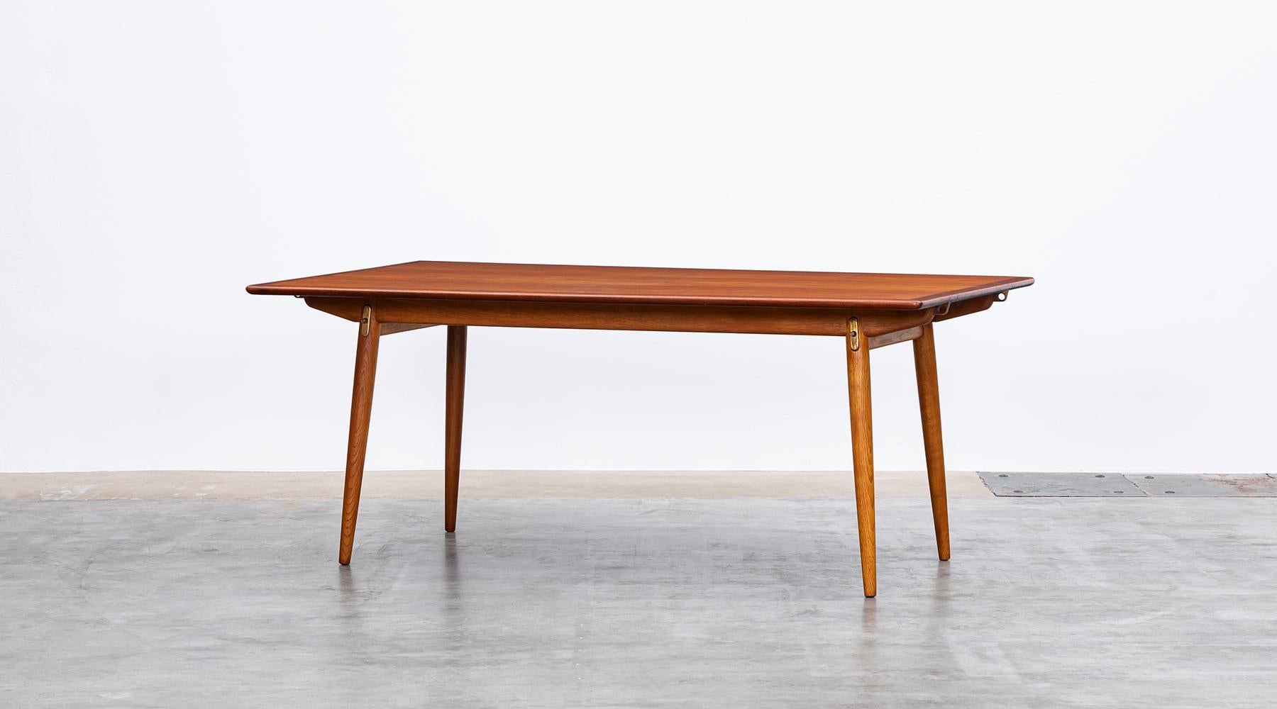 Stunning, solid dining table designed by Hans Wegner comes with a teak top on four oak legs and frame. The table is extendable to a maximum length of 297 cm. The details for use are in metal and brass. Manufactured by Johannes Hansen.

1936-38