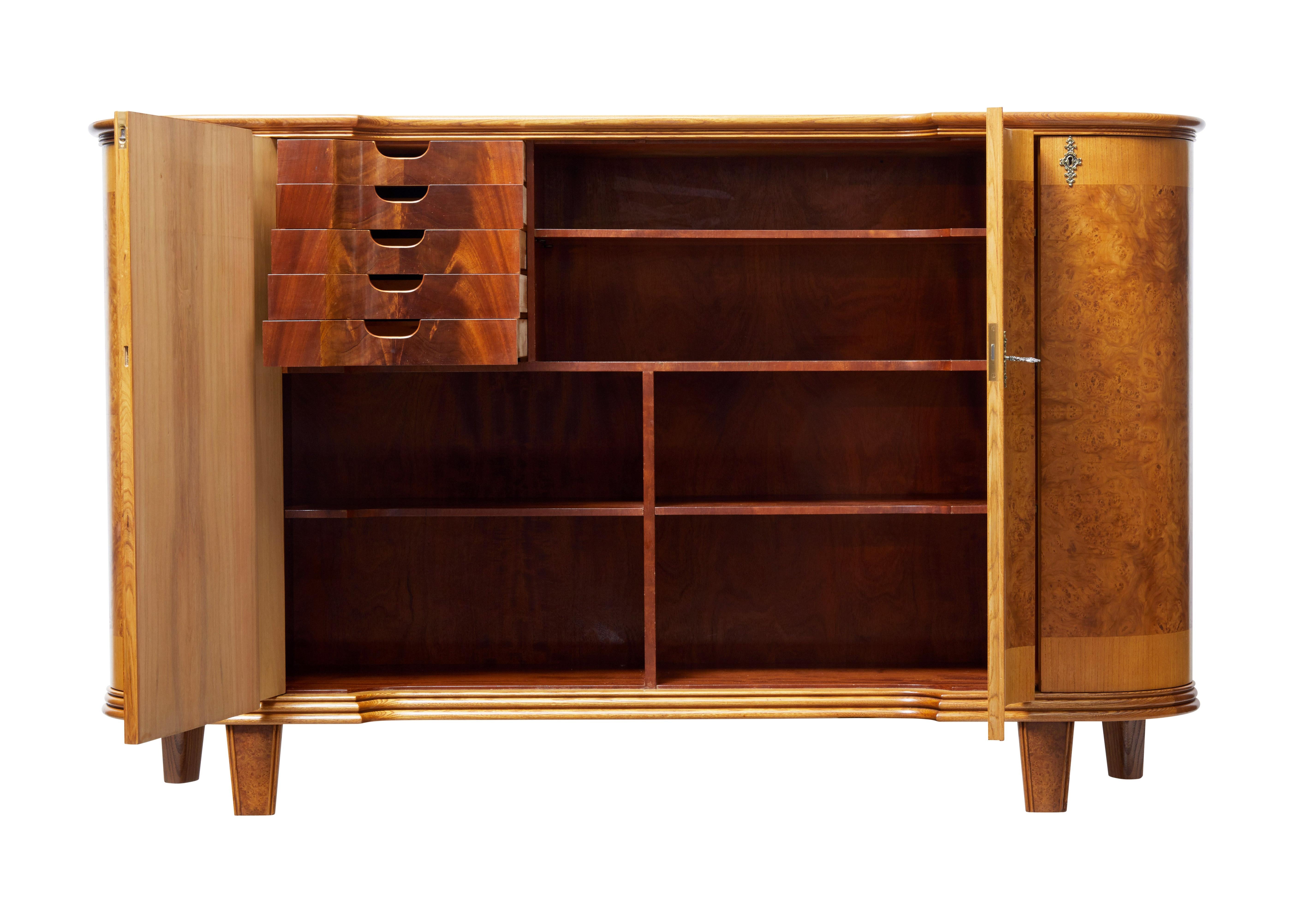 Fine quality mid-20th century elm sideboard.

Stunning shaped elm and burr elm 4 door sideboard. Fitted with ornate escutcheons and working key and locks. Central double doors open to reveal a partially fitted interior of contrasting color. A bank