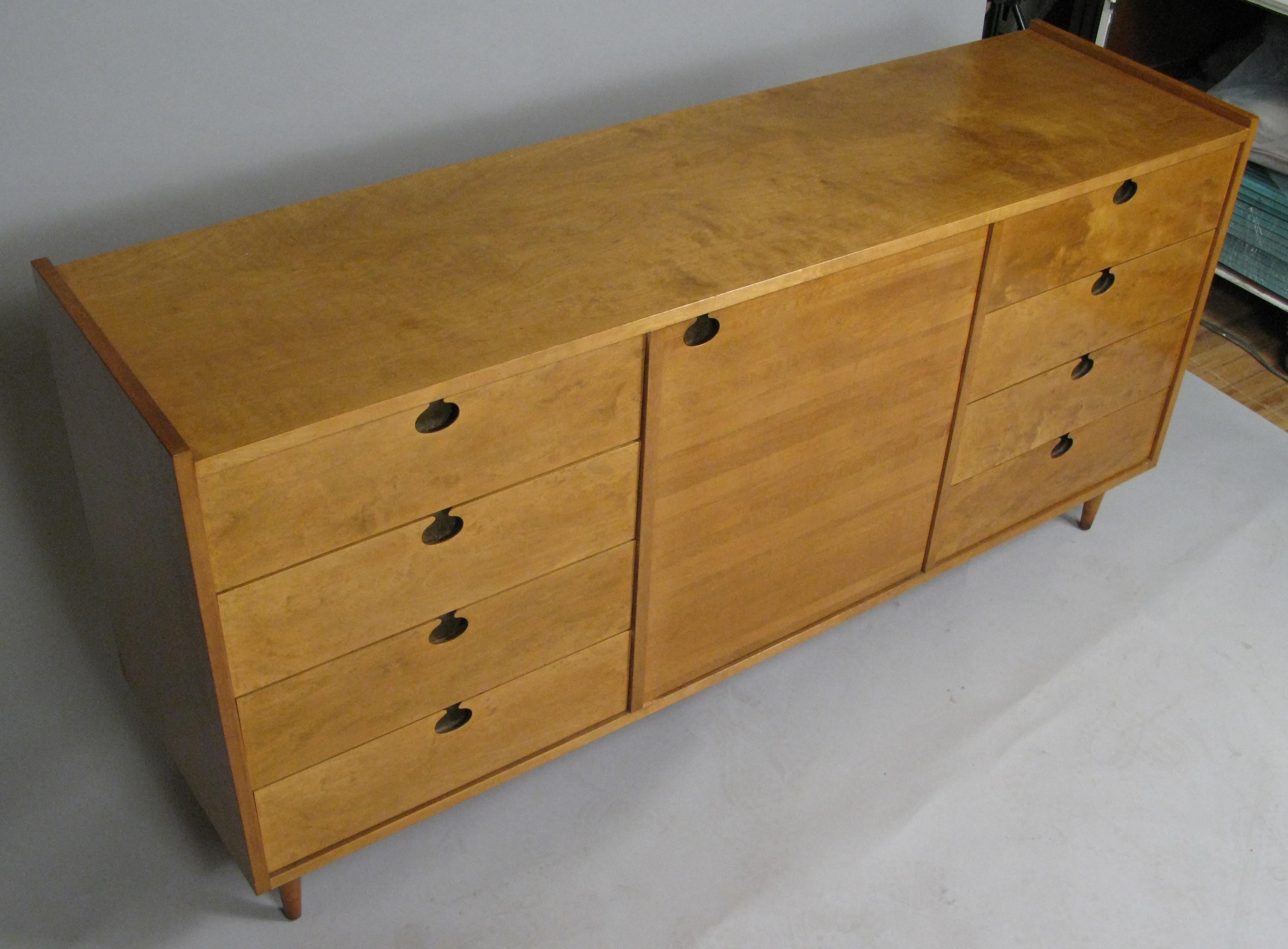 This 1950s Swedish maple sideboard / chest by Edmond Spence is composed of eight drawers (four on each side) divided by a centre storage section with two shelves. Each cabinet pull is inset brass, and the piece is supported by four two-tone maple,