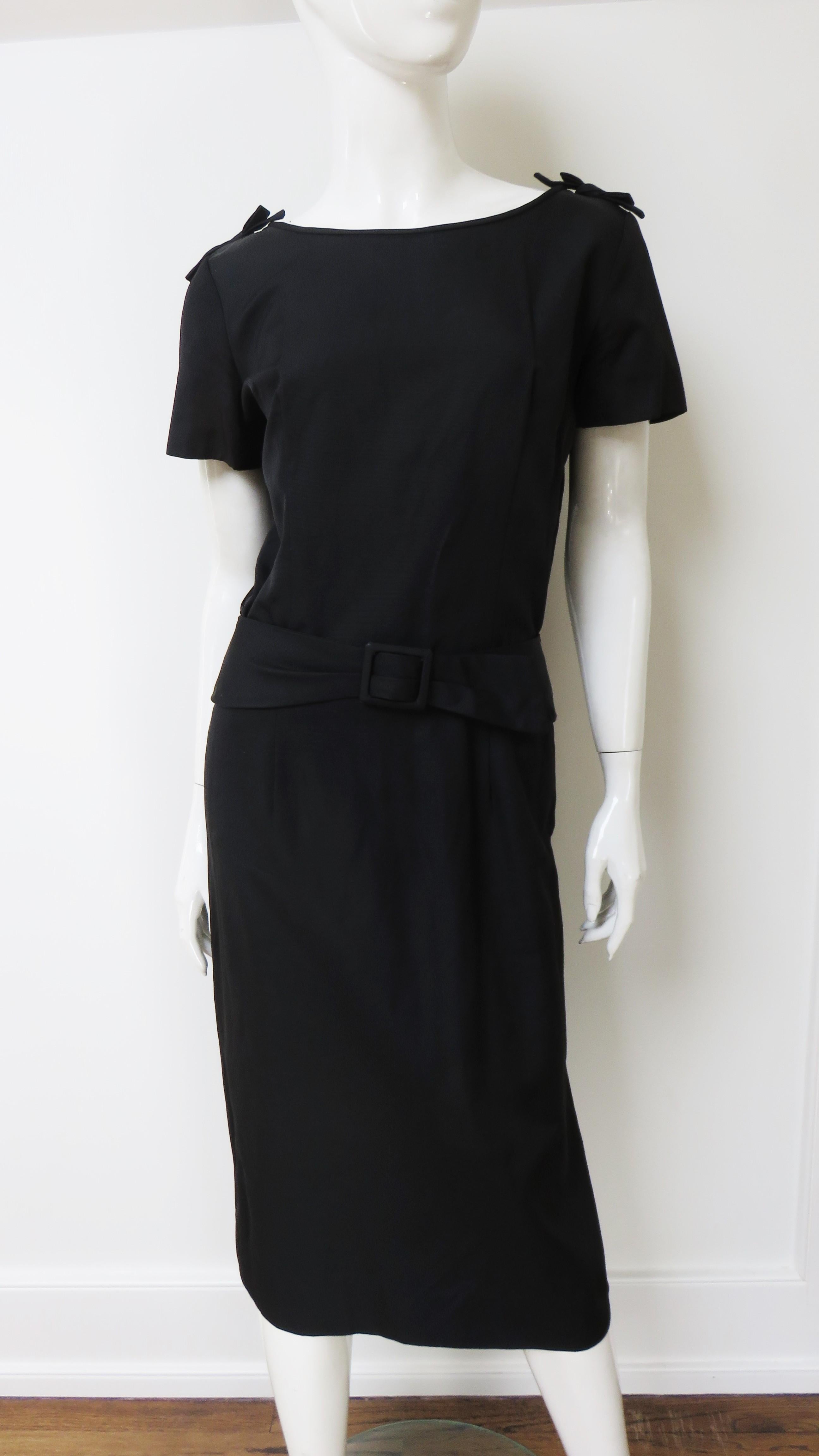 A great black dress with a bateau neckline, short sleeves and small vertical straps draping in the bodice back. It has a straight skirt with a back vent and an attached belt. The dress is unlined with a side metal zipper.
Fits size Medium.

Bust 