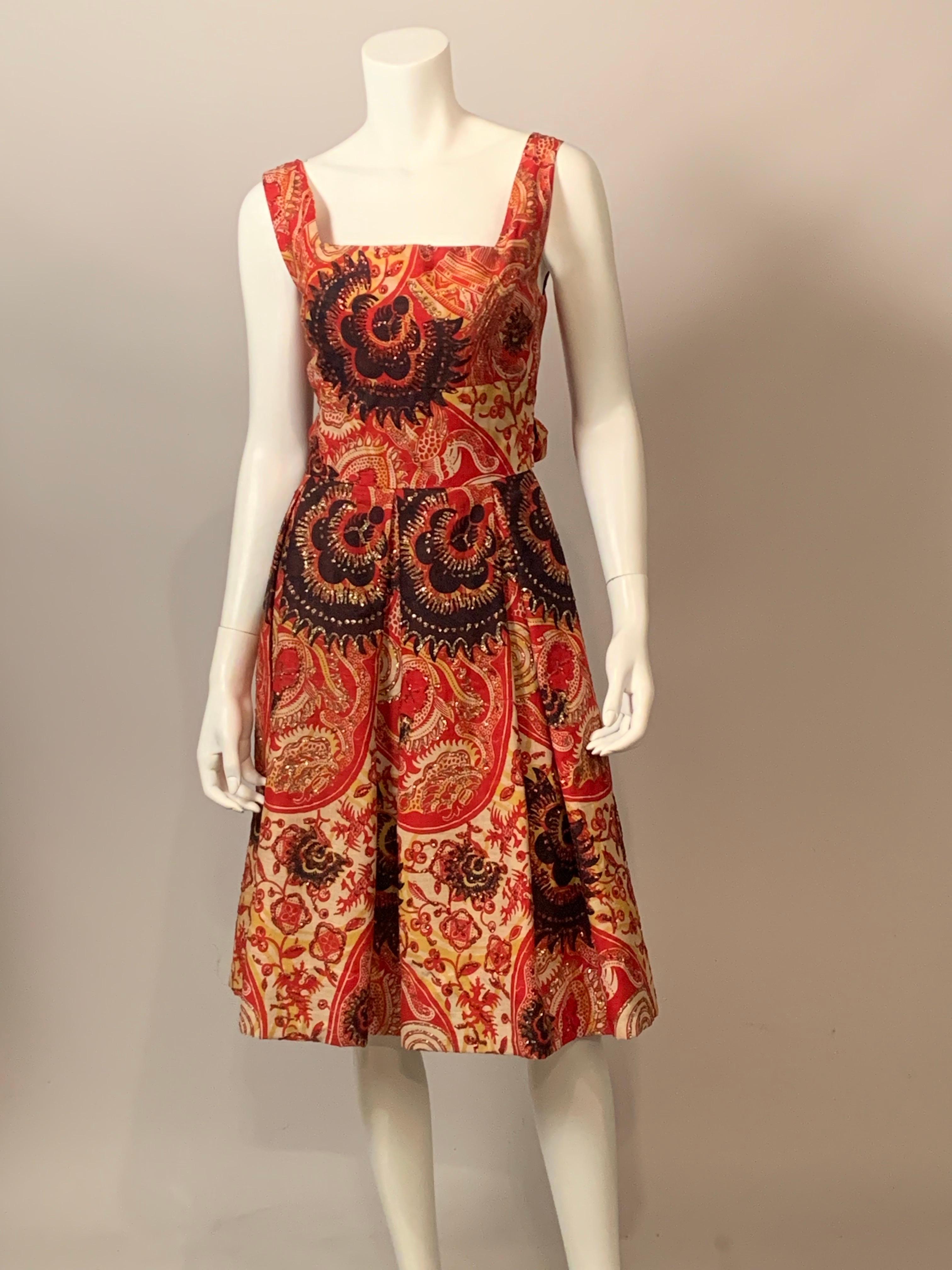 Calypso, di Bermuda e Montego Bay, ha disegnato questo favoloso abito anni '50 in cotone stampato nei toni del rosso, giallo, nero e bianco. Poi hanno aggiunto dei brillantini al disegno floreale. 
L'abito senza maniche ha una scollatura quadrata,