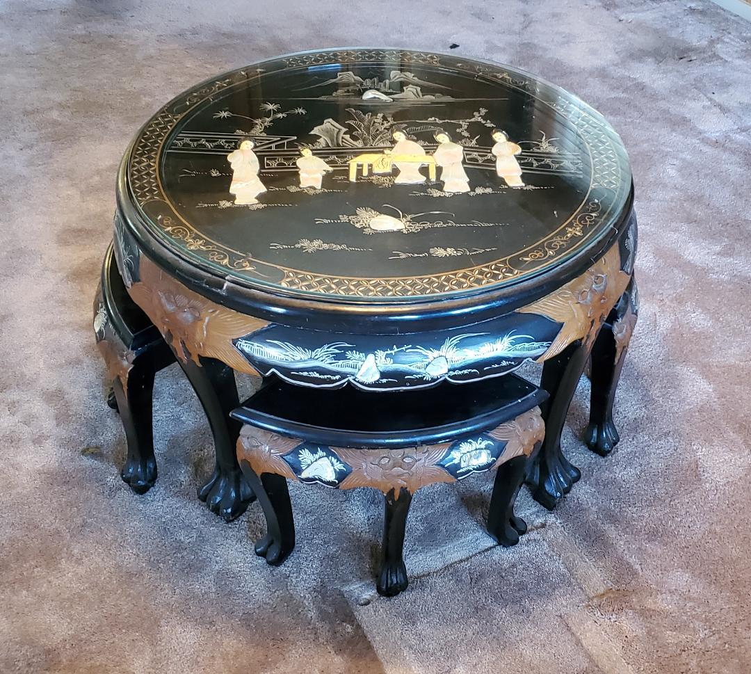 1950s Hand Carved Asian Tea Table With Matching Triangular Wedged Stools All Claw Footed.  
This Beautiful Vintage Black Lacquered Wooden Tea Table / Coffee Table With Mother Of Pearl Figural Inlay And Scenic Hand Painted Gold And Silver/White Motif