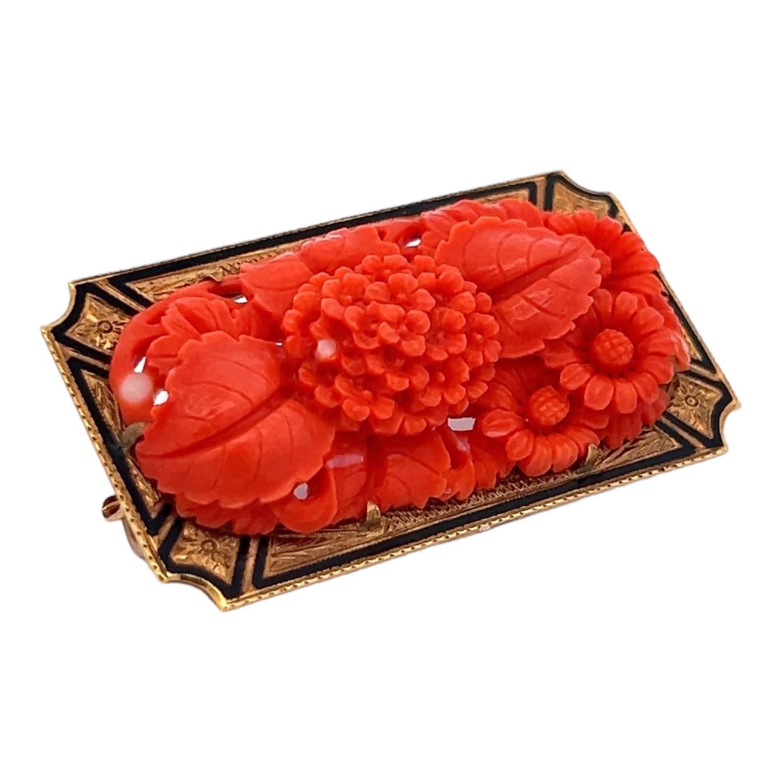 Beautifully carved coral and enamel brooch handcrafted in 18 karat yellow gold. The Mid-20th Century brooch features carved coral flowers and black enamel accents. The pin measures 4.50 x 2.50 inches. 