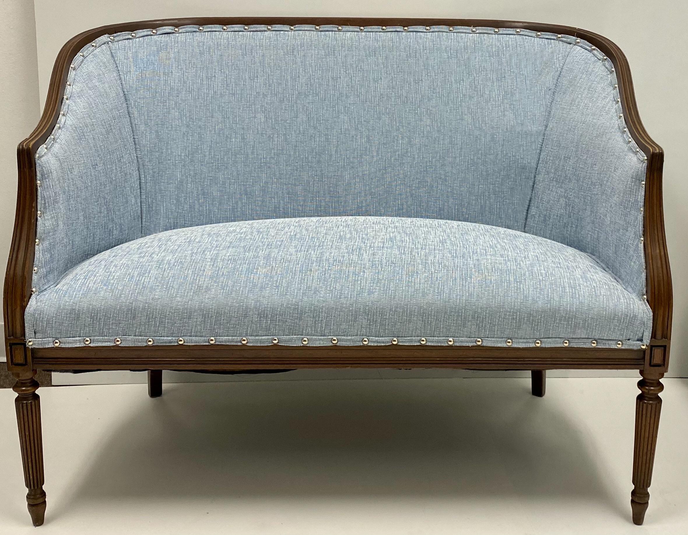 This is a 1950s Sheraton style carved mahogany settee. The blue upholstery and silver nailheads appear to be recent additions. The frame is carved mahogany with reeded and tapered legs.