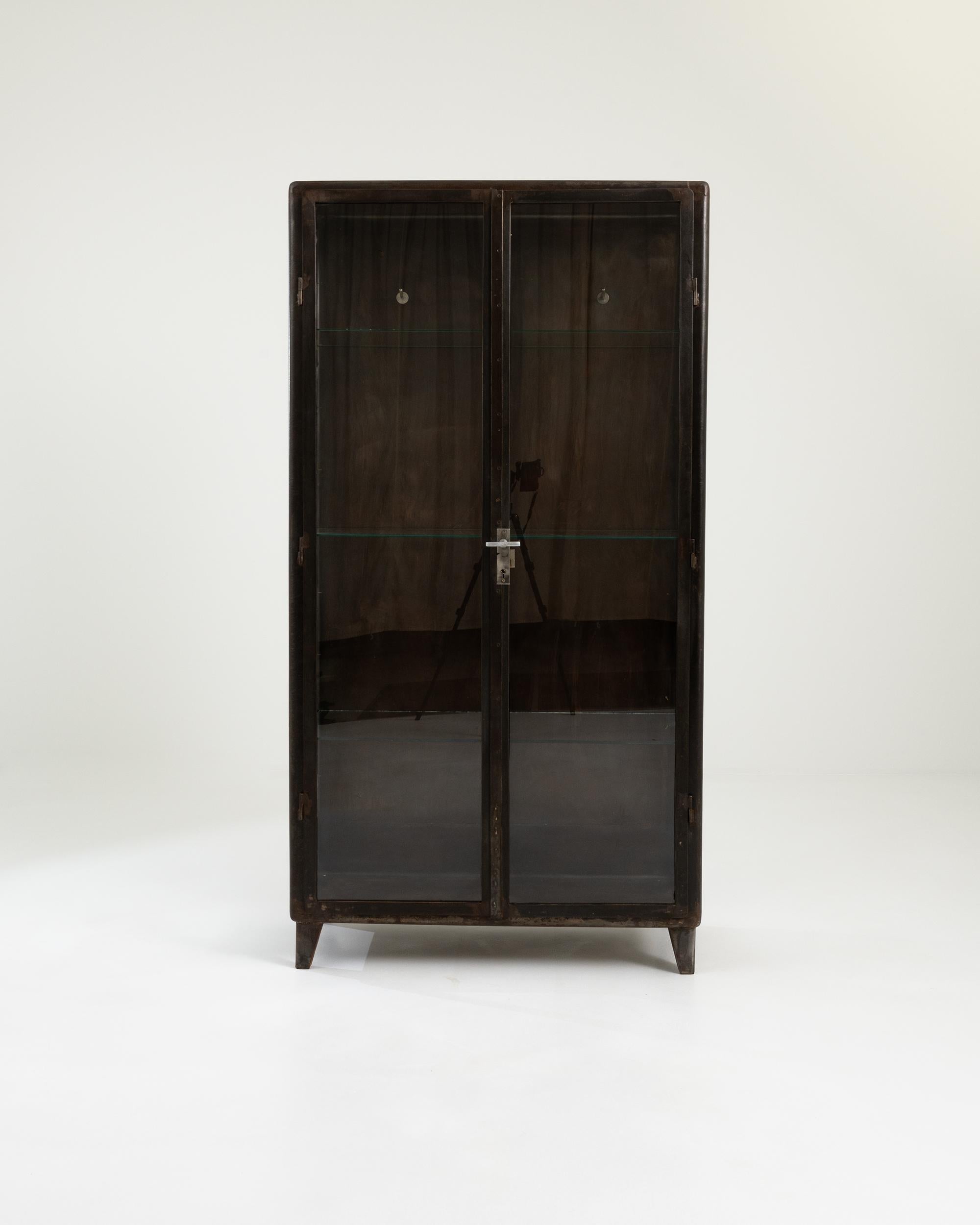 Designed to showcase medical equipment, this 1950s Central European vitrine is primarily constructed with glass panels, including front doors, sides, and shelves, to ensure maximum visibility. The polished metal frame, with its rich dark brown hue,