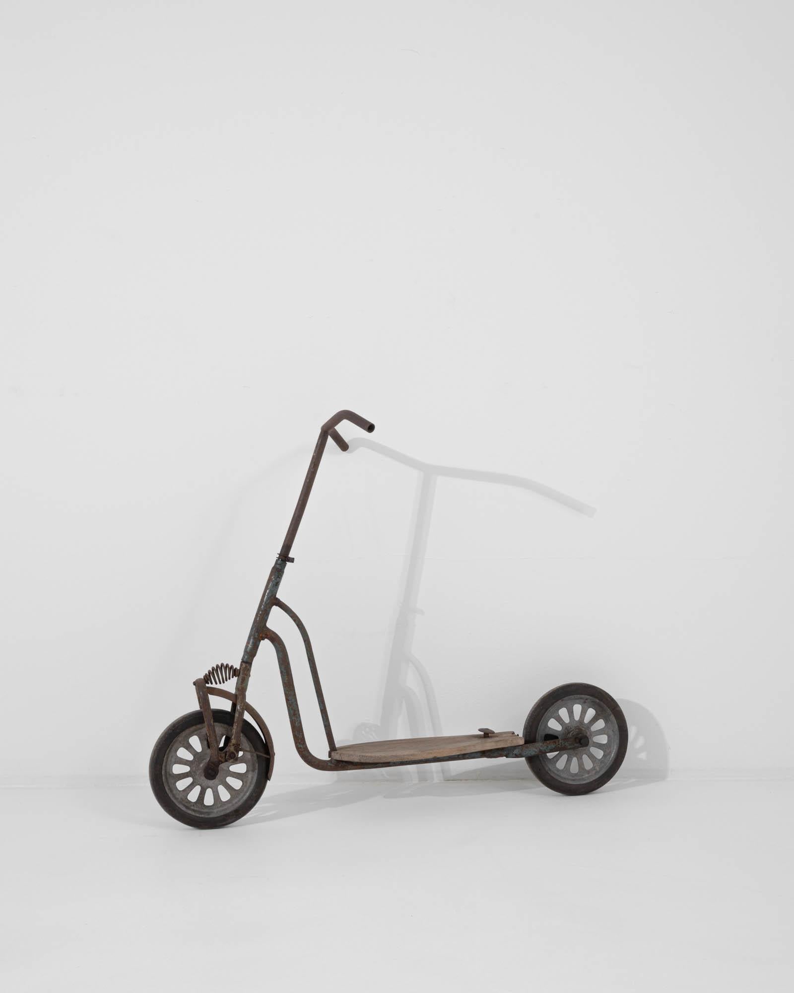 Step back in time with this authentic 1950s Central European Metal and Wooden Scooter, a whimsical piece that captures the playful spirit of yesteryears. Its sturdy construction features a combination of robust metal and solid wood, telling the tale
