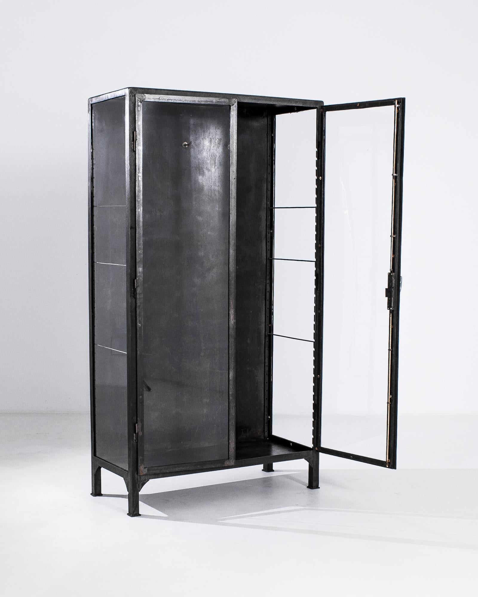 A metal display cabinet from 1950s Central Europe. Welded metal joinery, smoothed at the corners forms a utilitarian but eye-pleasing framing for this cabinet’s delicately composed glass shelves and drawers. Created with industrial mid-century