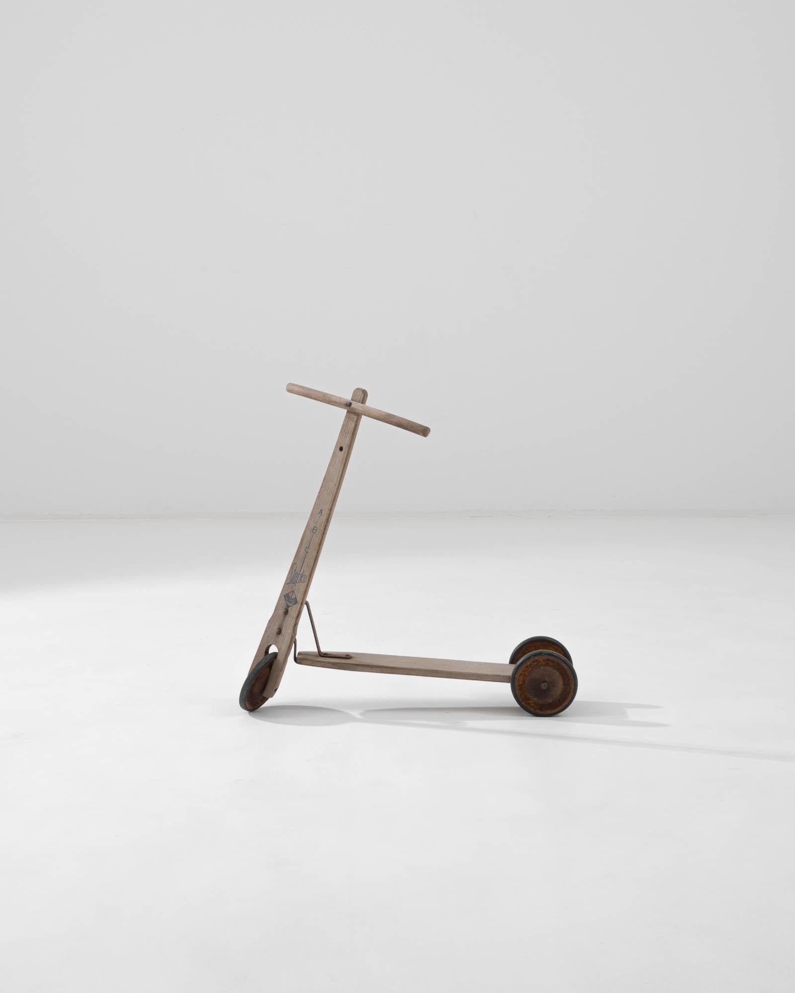 Introducing the 1950s Central European Metal & Wooden Scooter – a delightful piece of post-war history that captures the essence of childhood fun from a simpler time. This charming scooter is expertly crafted from solid wood and metal, featuring a