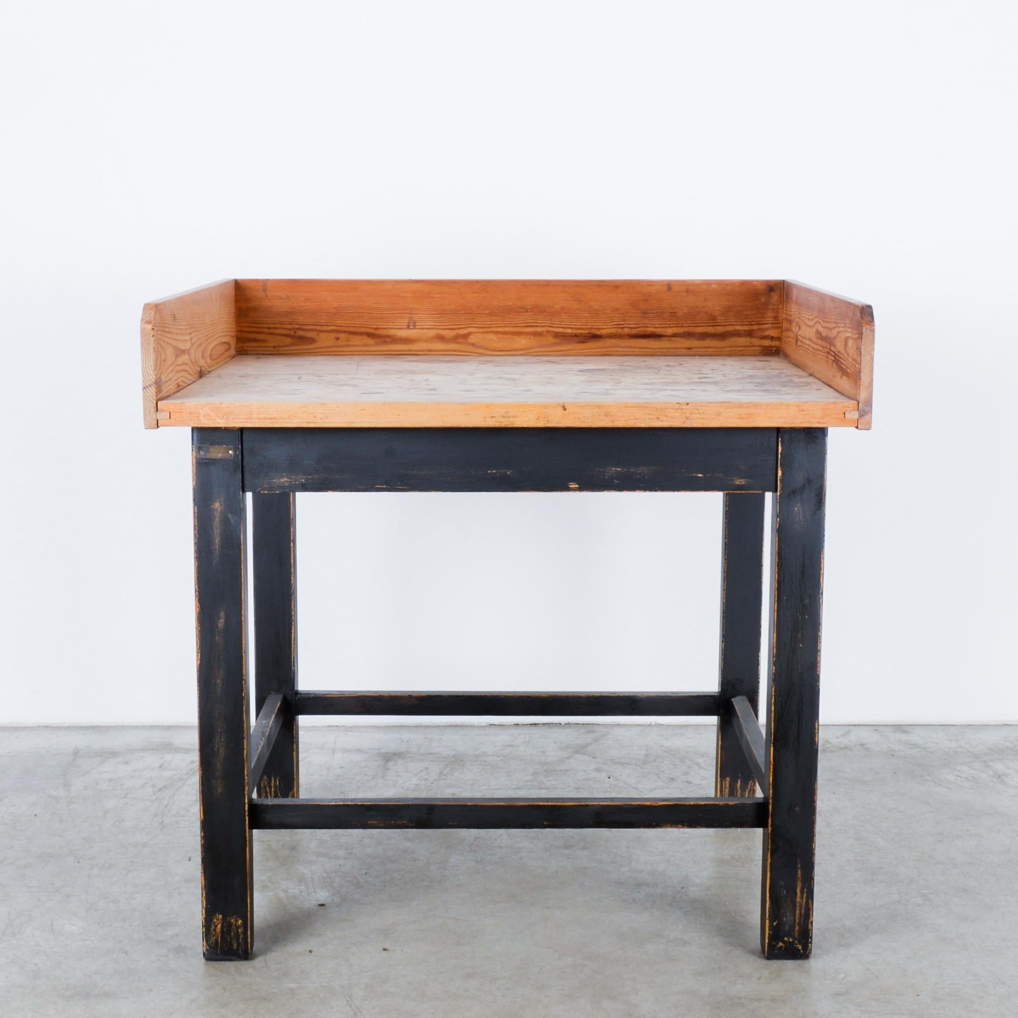 Ein hölzerner Bäckertisch aus Mitteleuropa, um 1950. Ein quadratischer, schwarz lackierter Rahmen trägt eine Arbeitsplatte aus Naturholz. Holzpaneele an drei Seiten der Tischplatte bilden einen geschlossenen Arbeitsbereich, ein praktischer Aspekt,