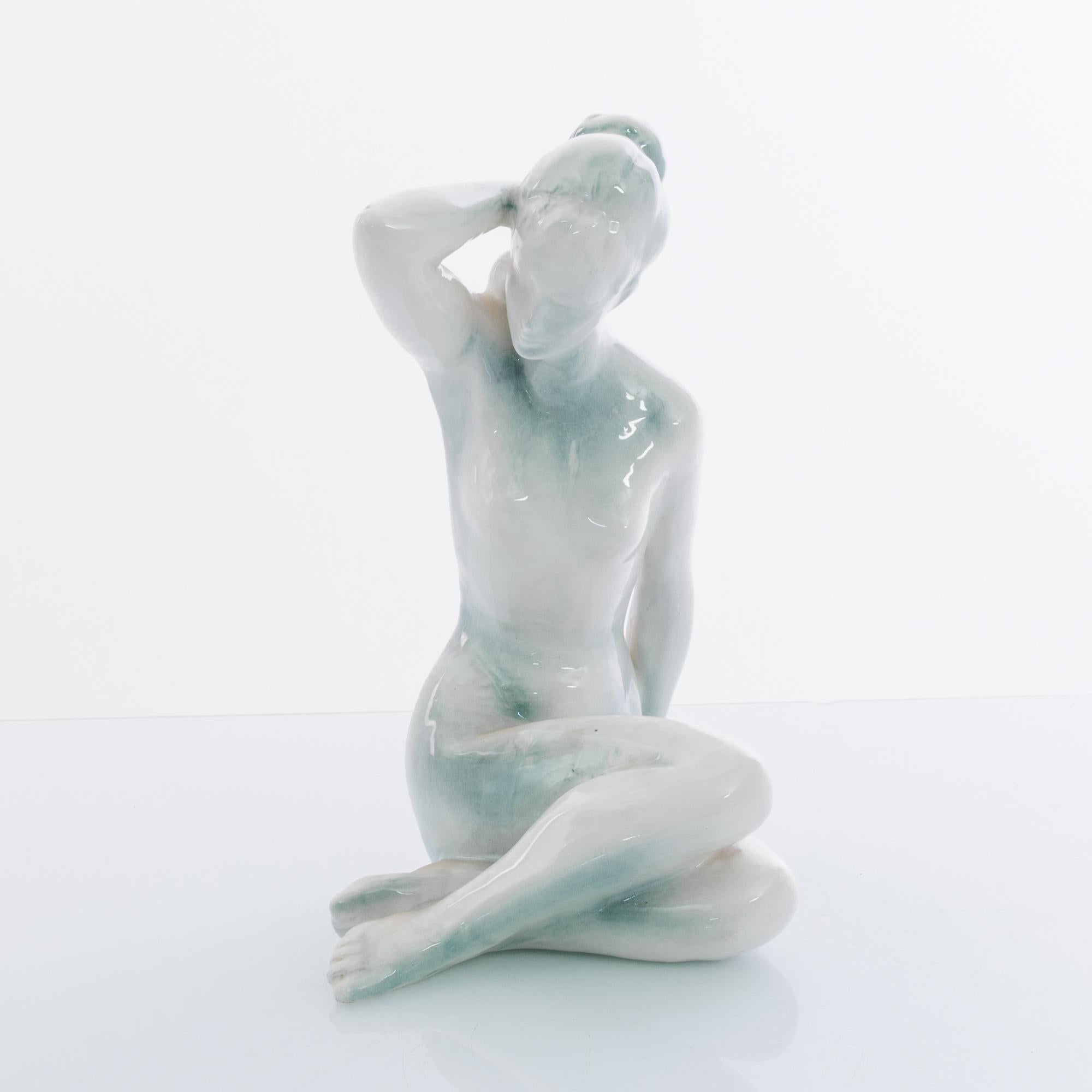 A ceramic statue from Czechia, circa 1950, depicted a naked woman. The natural pose and glossy glaze of the white ceramic create an impression of calm and simplicity; the shadow of blue glaze which runs across the surface gives depth and definition