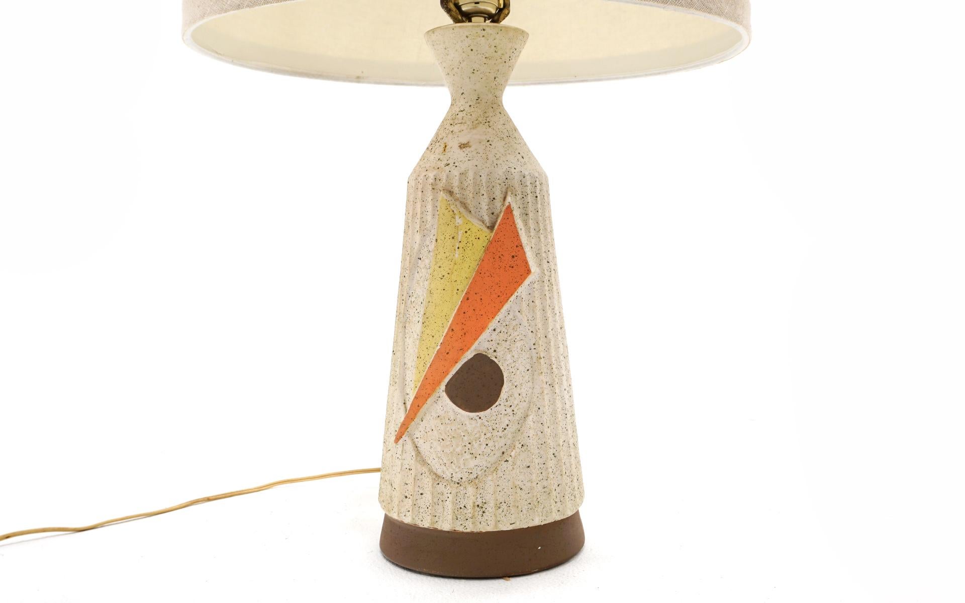 Ceramic table lamp in off white with abstract orange, yellow and brown design. Similar in style to lamps designed by Gordon and Jane Martz for Marshall Studios. Comes with the original shade. Very good condition with no chips, cracks, or repairs.