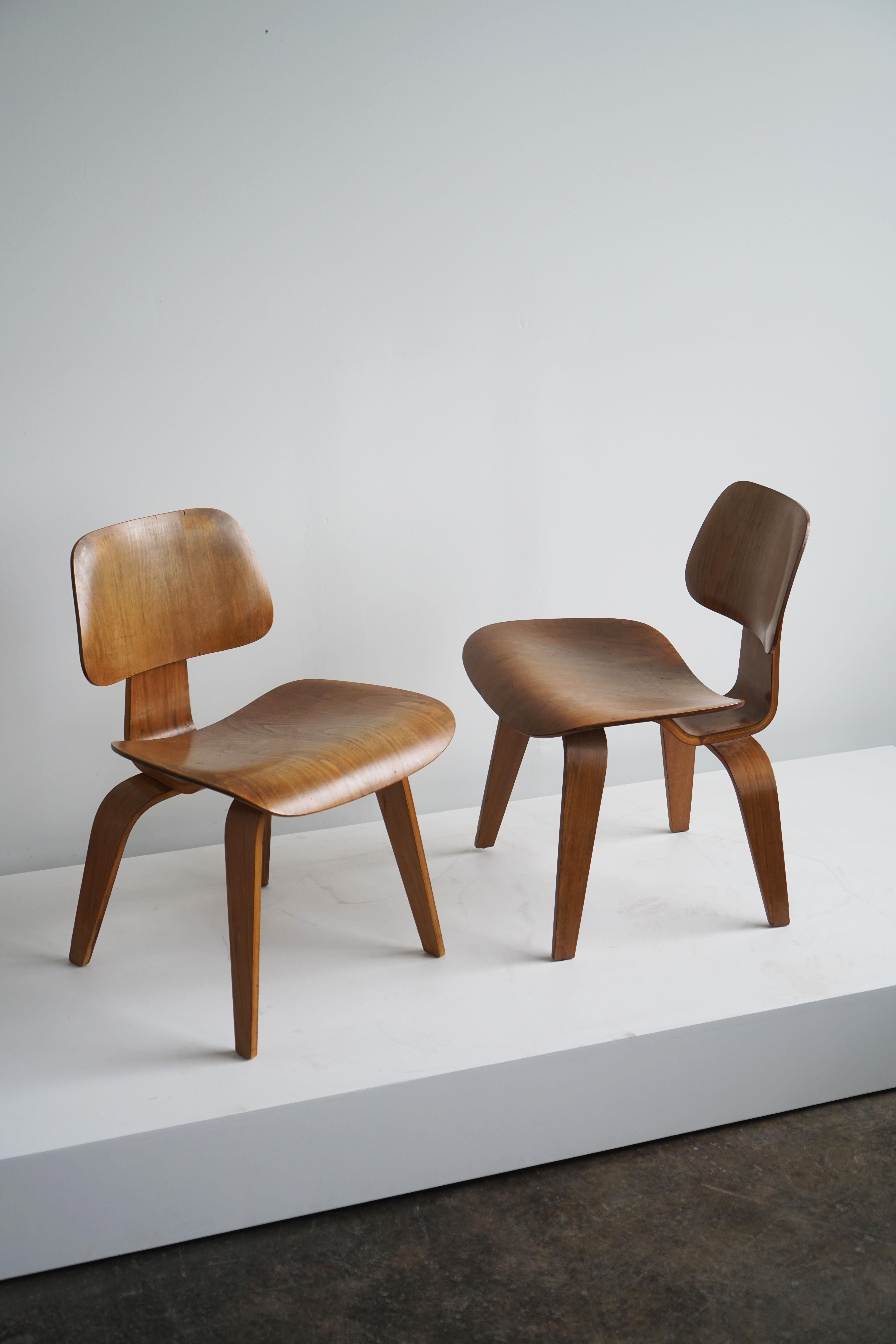 Charles and Ray Eames, 
DCW plywood chairs, pair.

Herman Miller, USA
Circa 1950
Walnut plywood.

These chairs are 2nd generation (1st generation Herman Miller) as identified by the 5-2-4 screw pattern on the base and the rounded feet.

The