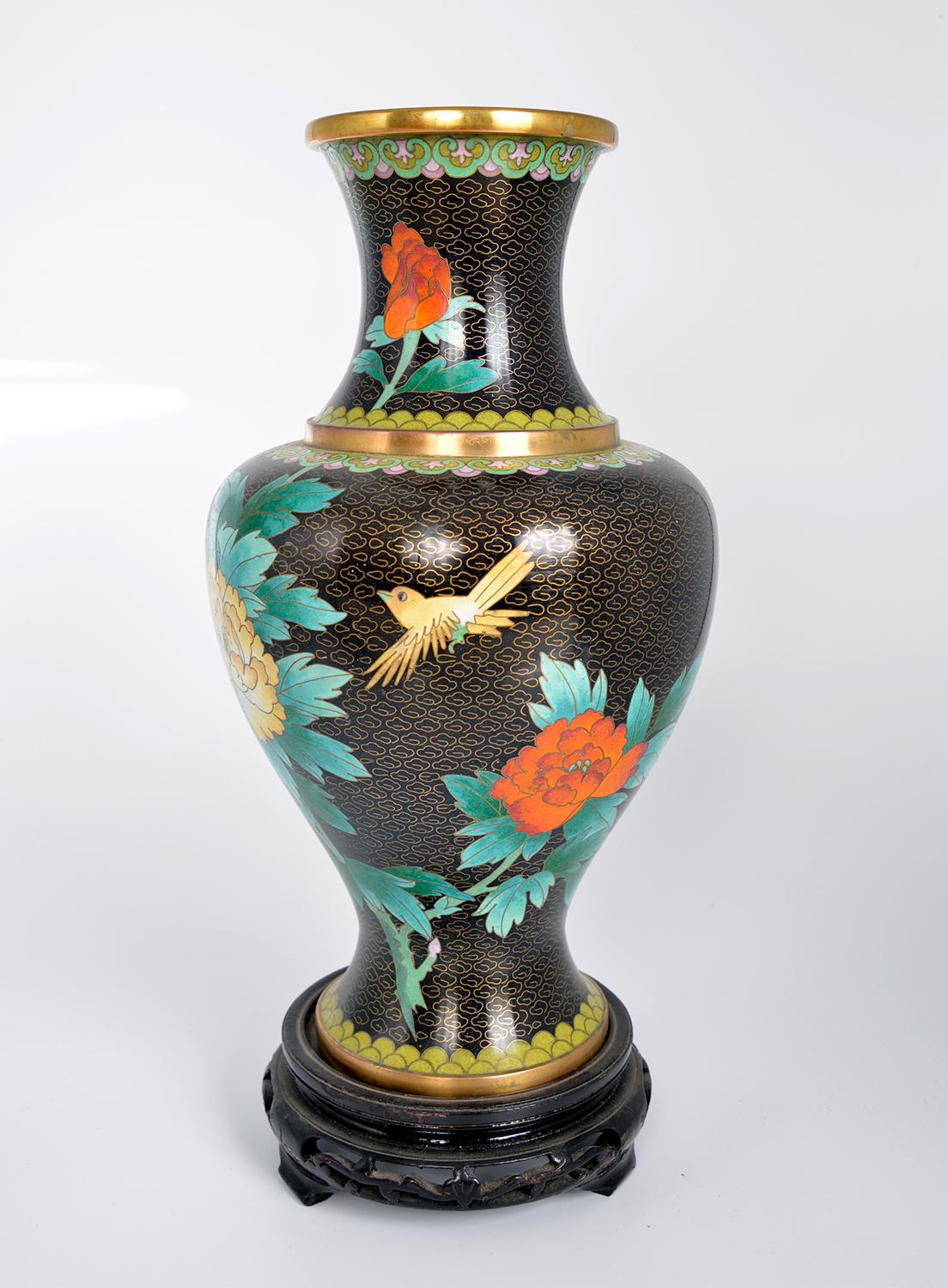Chinese enamel and brass Zi Jin Cheng floral cloisonné vase that sits on a carved ebonised wooden stand. The vase has a black and gold background featuring various flowers and foliage in rich colours, including a lotus flower, rose, carnation and a