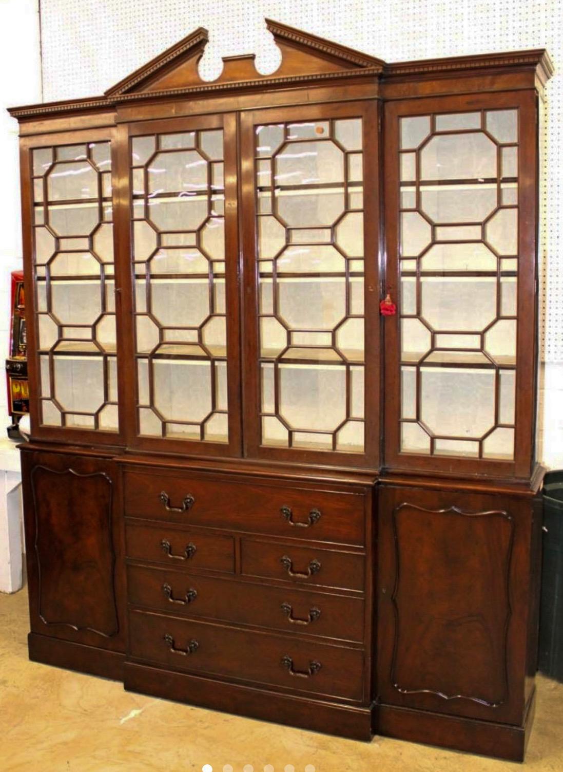 This is such a lovely breakfront. It was manufactured in New York. 
Note the broken arch pediment! The front has the drop down revealing a leather surface to give it the functionality of a secretarie. The piece is lined with damask that does show