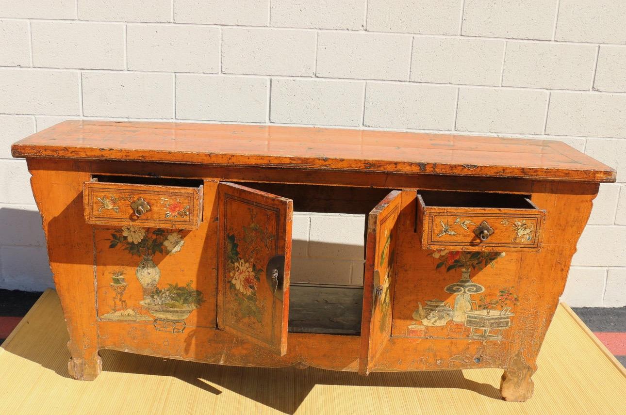 Wonderful vintage Chinese hand painted credenza made of teakwood. From the 1950’s. This piece features an orange color finish hand painting of fruits & flowers. It has two front drawers, and two center doors. Also, it comes with brass handles. It