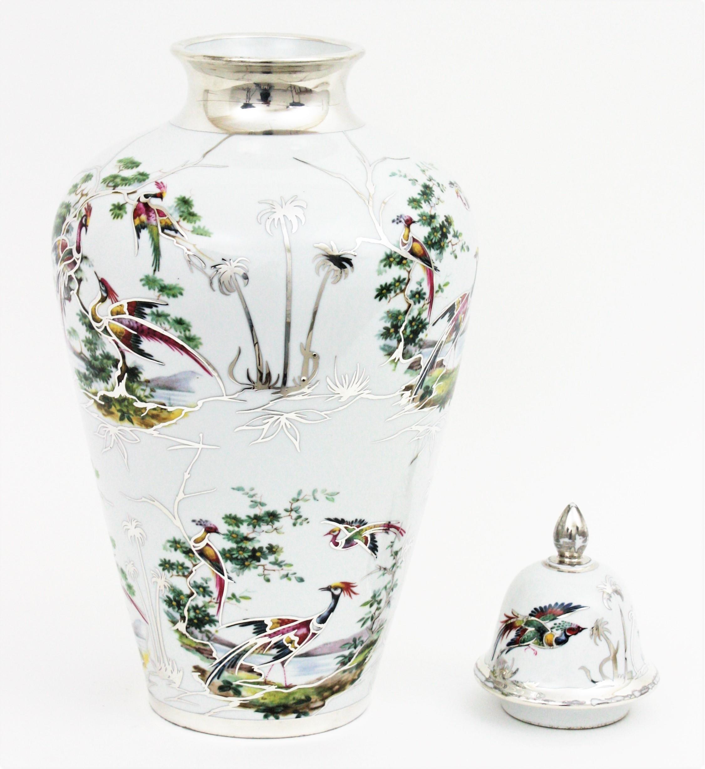 Mid-Century Modern porcelain tall vase with lid, floral and naturalistic motifs, China, 1940s-1950s.
This urn lidded vase features a naturalistic landscape with birds, trees and plants on a white background accented by hand painted silver