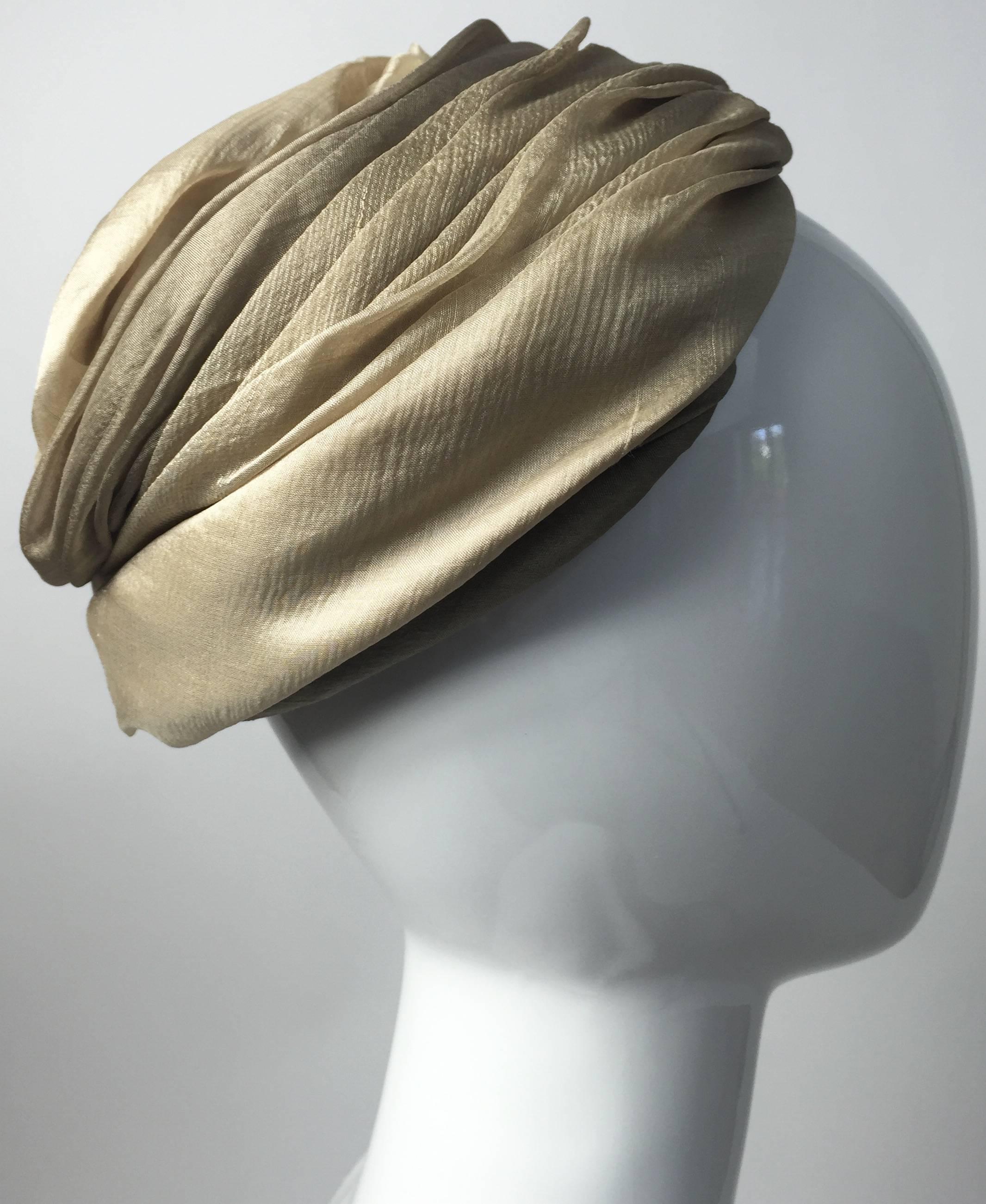 Un exquis chapeau turban Christian Dior du début des années 1950. Réalisé en mousseline de soie douce dans des tons taupe, beige et ivoire clair et doré. Le tissu est légèrement drapé et plissé. Finition à la main. Doublé d'un filet
En excellent