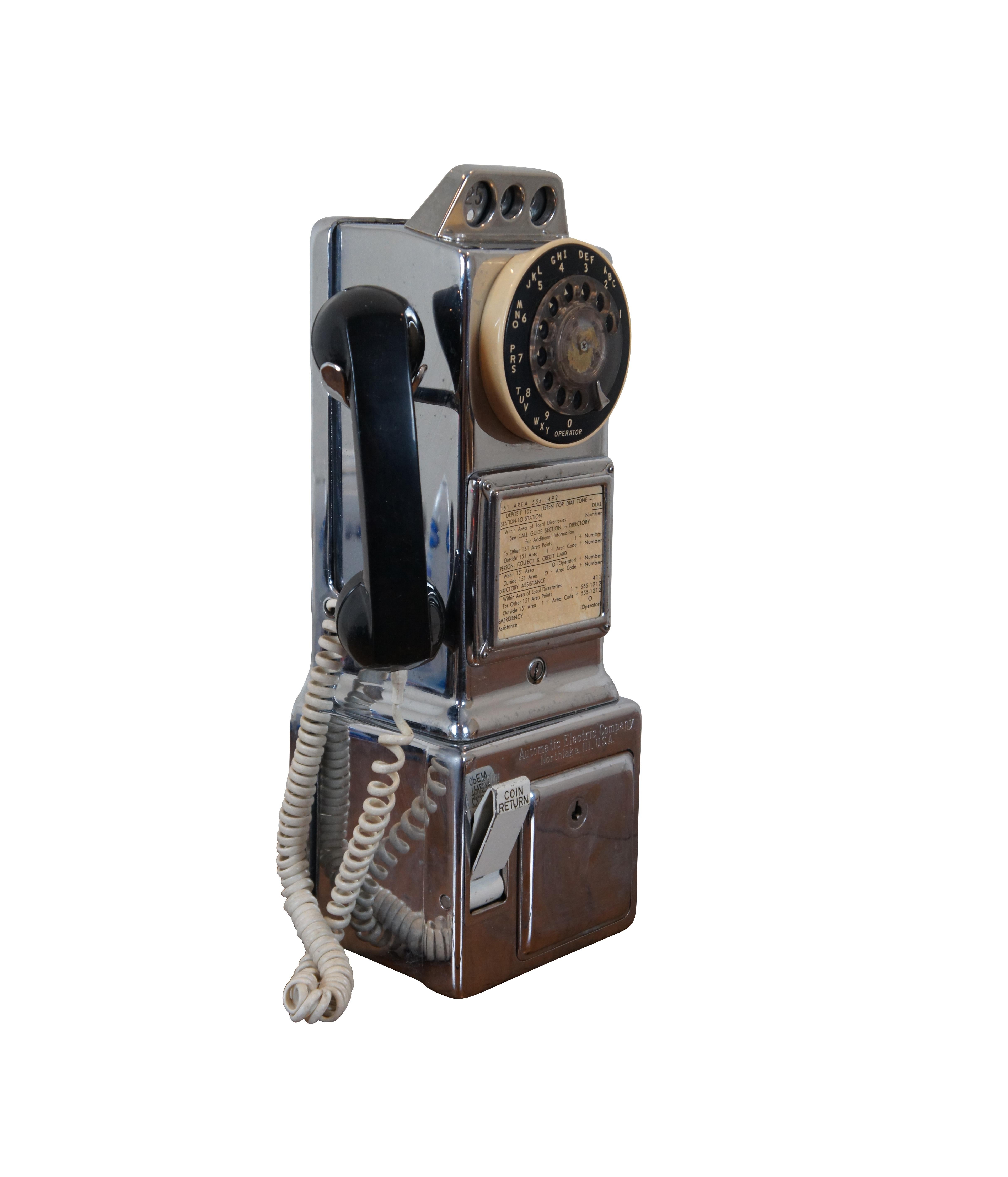 Vintage 1950s wall mounted pay phone / telephone by the Automatic Electric Company, with three coin slots, rotary dial, and black plastic receiver. Measure: 18
