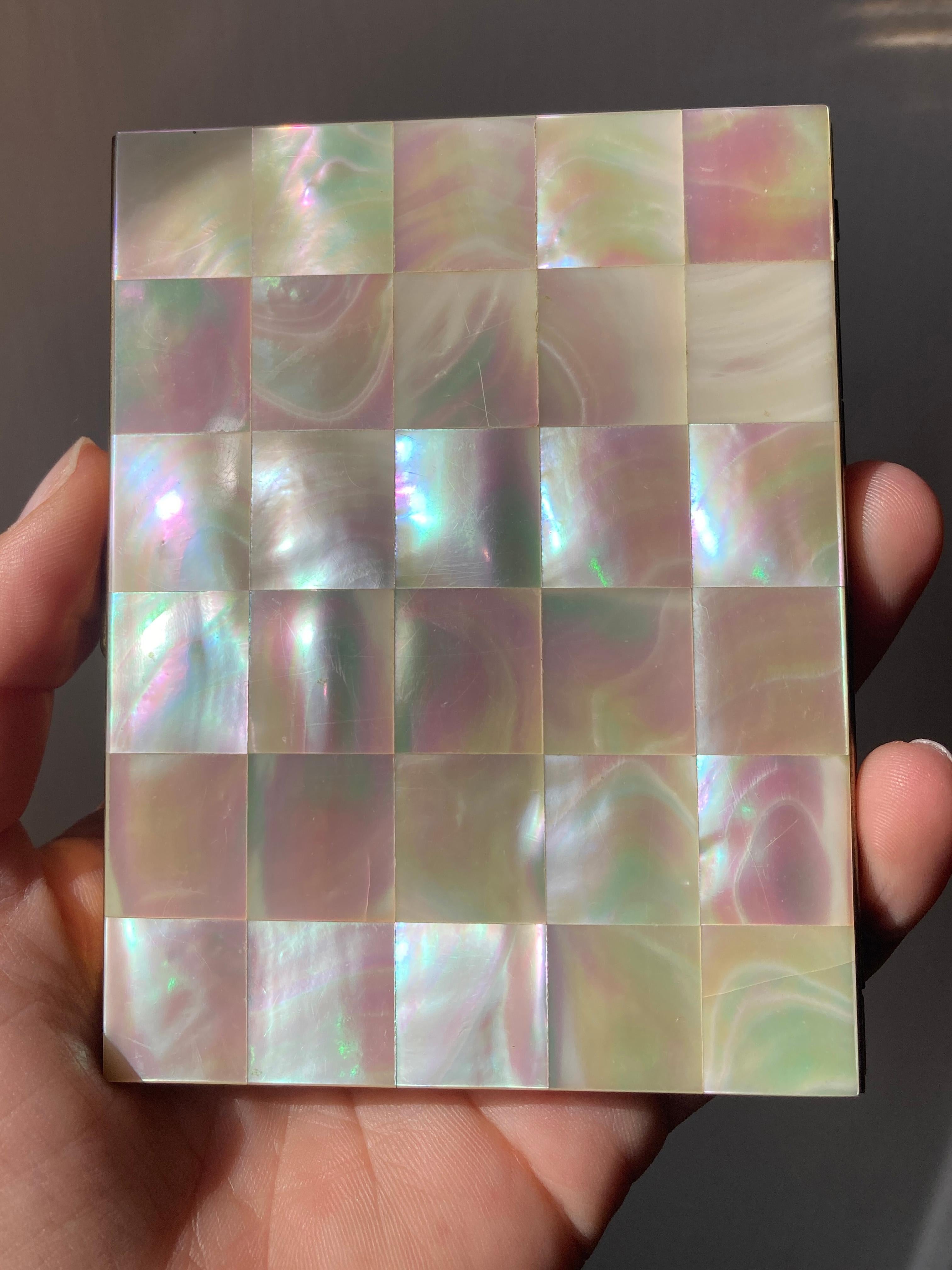 This 1950s cigarette case Mother of pearl, is a true vintage treasure, crafted from 24K gold-plated metal for an opulent touch. Its exterior boasts a sophisticated design featuring mother-of-pearl arranged in a classic checkerboard pattern, adding a