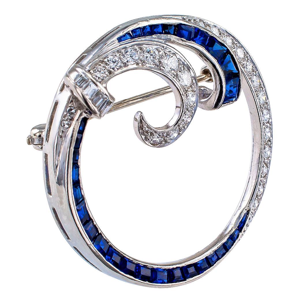 Mid century sapphire diamond and platinum circle brooch circa 1950. The design features contrasting courses of calibrated cut blue sapphires and round brilliant-cut diamonds, together blending into scrolling motifs on the upper half of the circle,