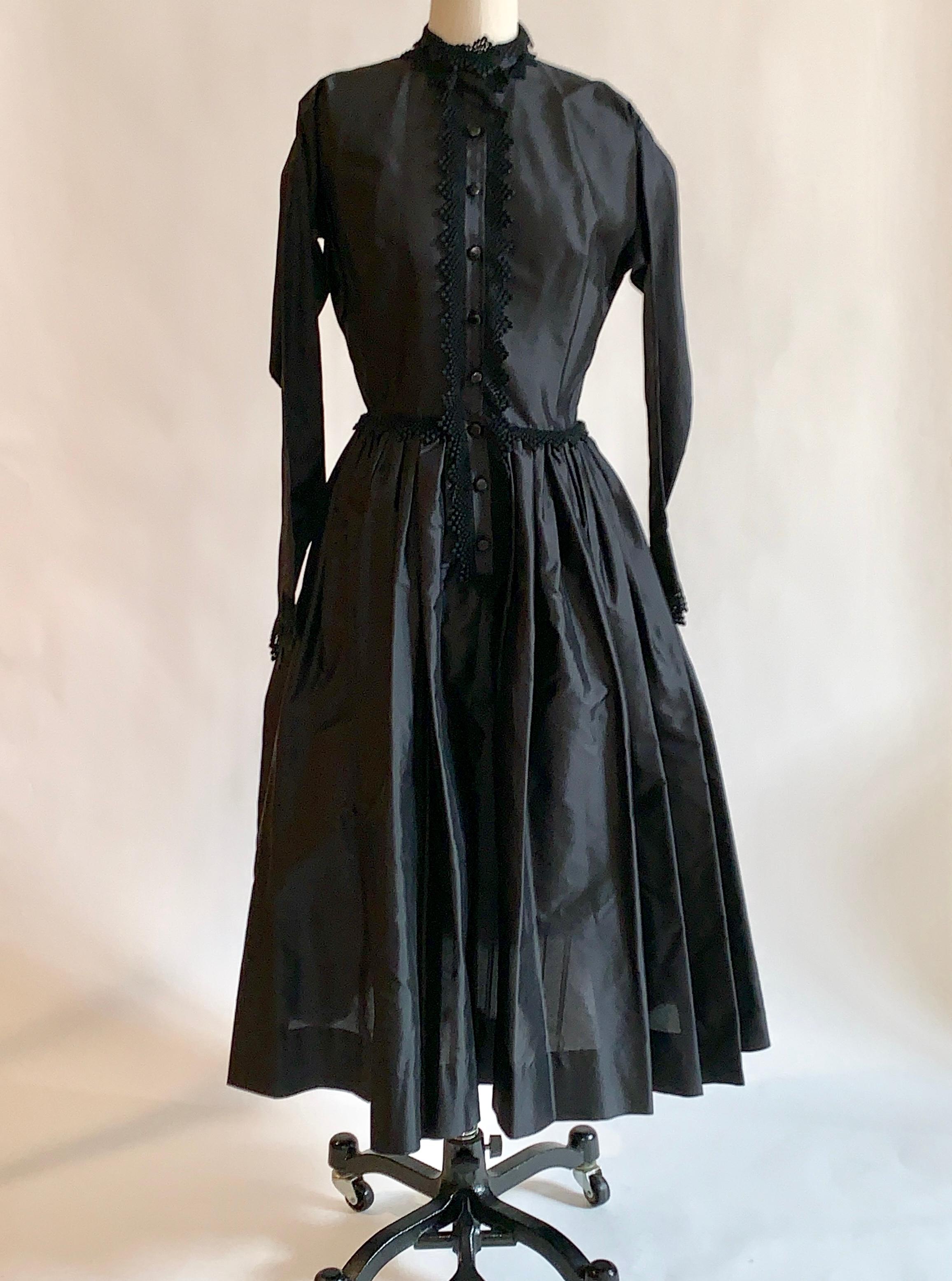 Claire McCardell for Townley 1950s black dress with shirt style top, full skirt, and long sleeves. Lace trim at placket, cuffs, and collar. Cuffs can be folded up at wrist, or worn so that the pointed cuff covers the palm. Closes with buttons at